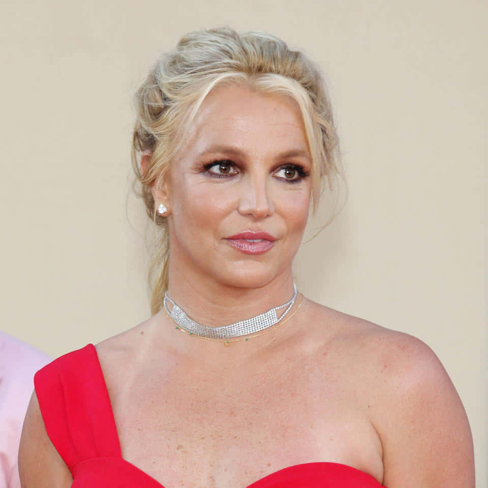 Britney Spears 桌布 壁紙 — 布蘭妮·斯皮爾斯在正式活動中穿著大膽的紅色單肩禮服，搭配閃閃發光的頸鍊。