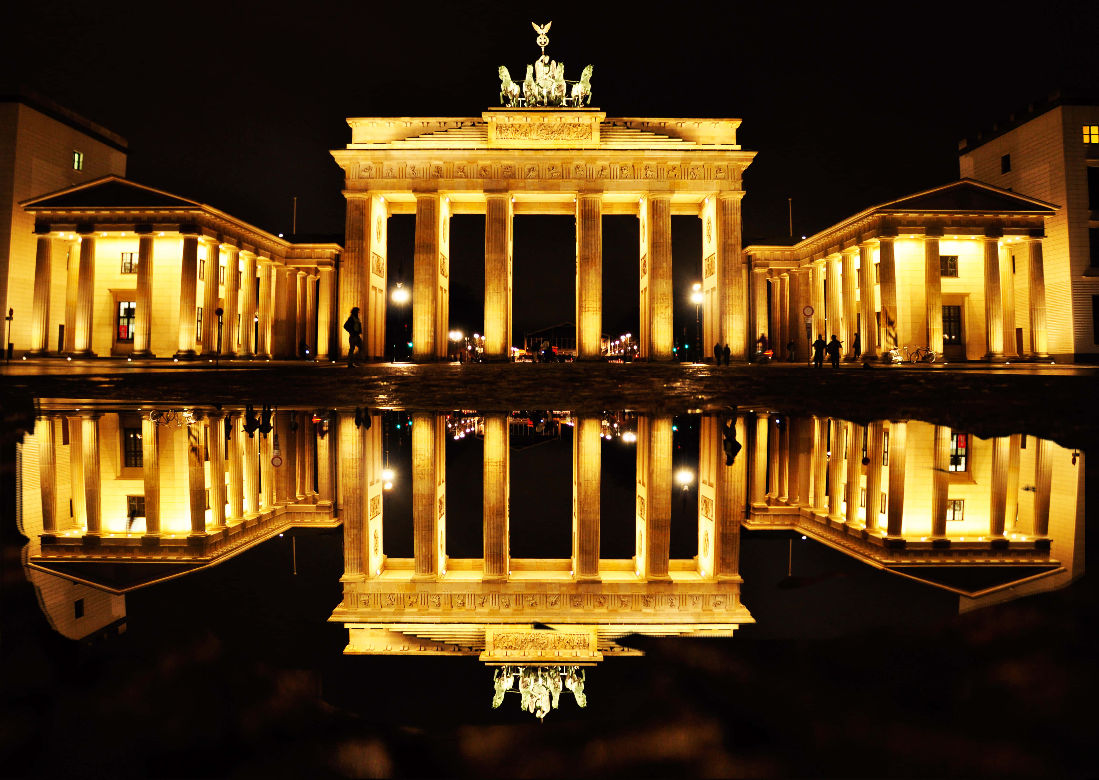 Berlin 桌布 壁紙 — 布蘭登堡門在夜晚溫暖地發光，其宏偉的新古典主義柱子在下面的水坑中完美倒映。
