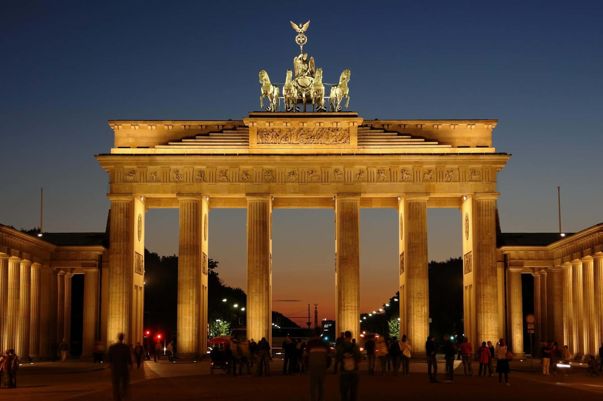 Berlin 桌布 壁紙 — 布蘭登堡門在黃昏時被金色燈光照亮，溫暖的光芒灑在其新古典主義柱子和頂部的四馬戰車雕像上。