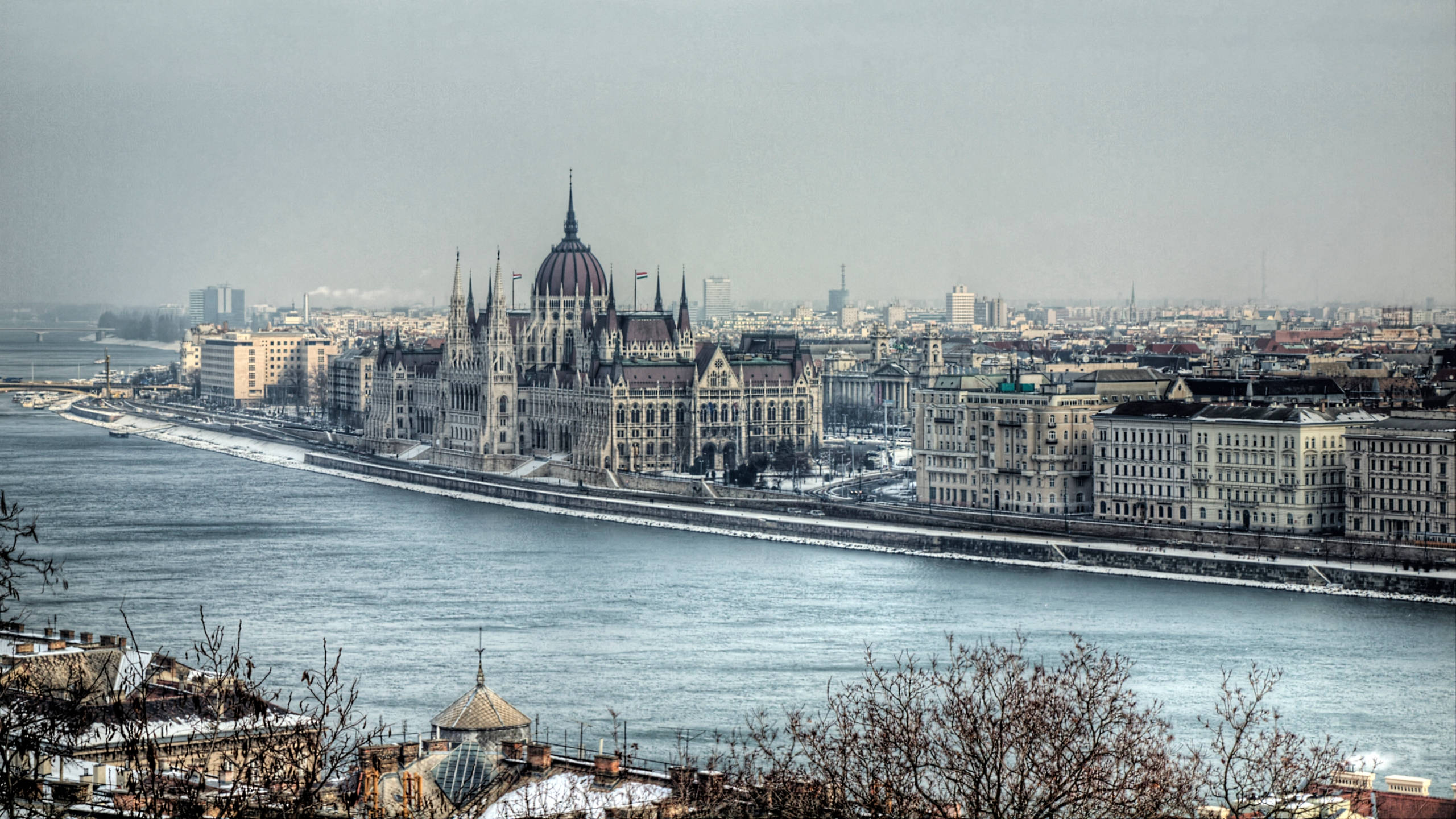 Hungary 桌布 壁紙 — 布達佩斯國會大廈沿多瑙河的 panoramatic 景觀，在朦朧的天空下，屋頂上覆蓋著雪。