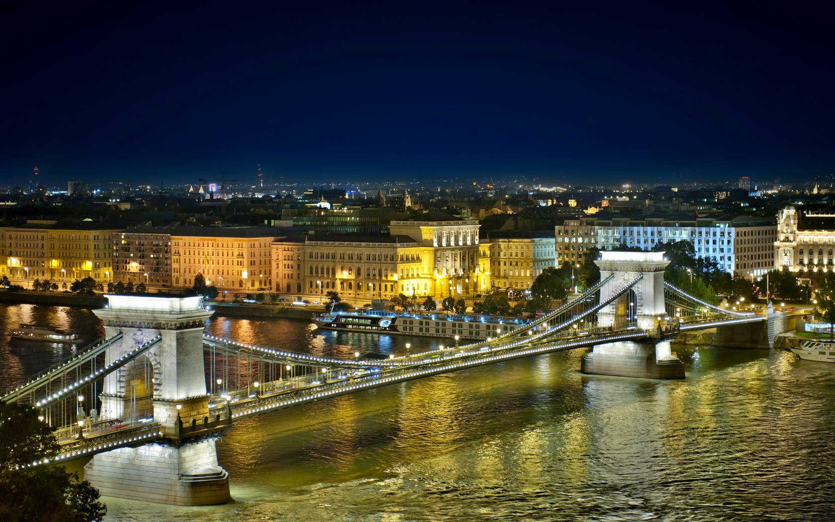 Hungary 桌布 壁紙 — 布達佩斯多瑙河上燈火通明的鏈橋的壯麗夜景，城市燈光在水面上閃爍倒映。