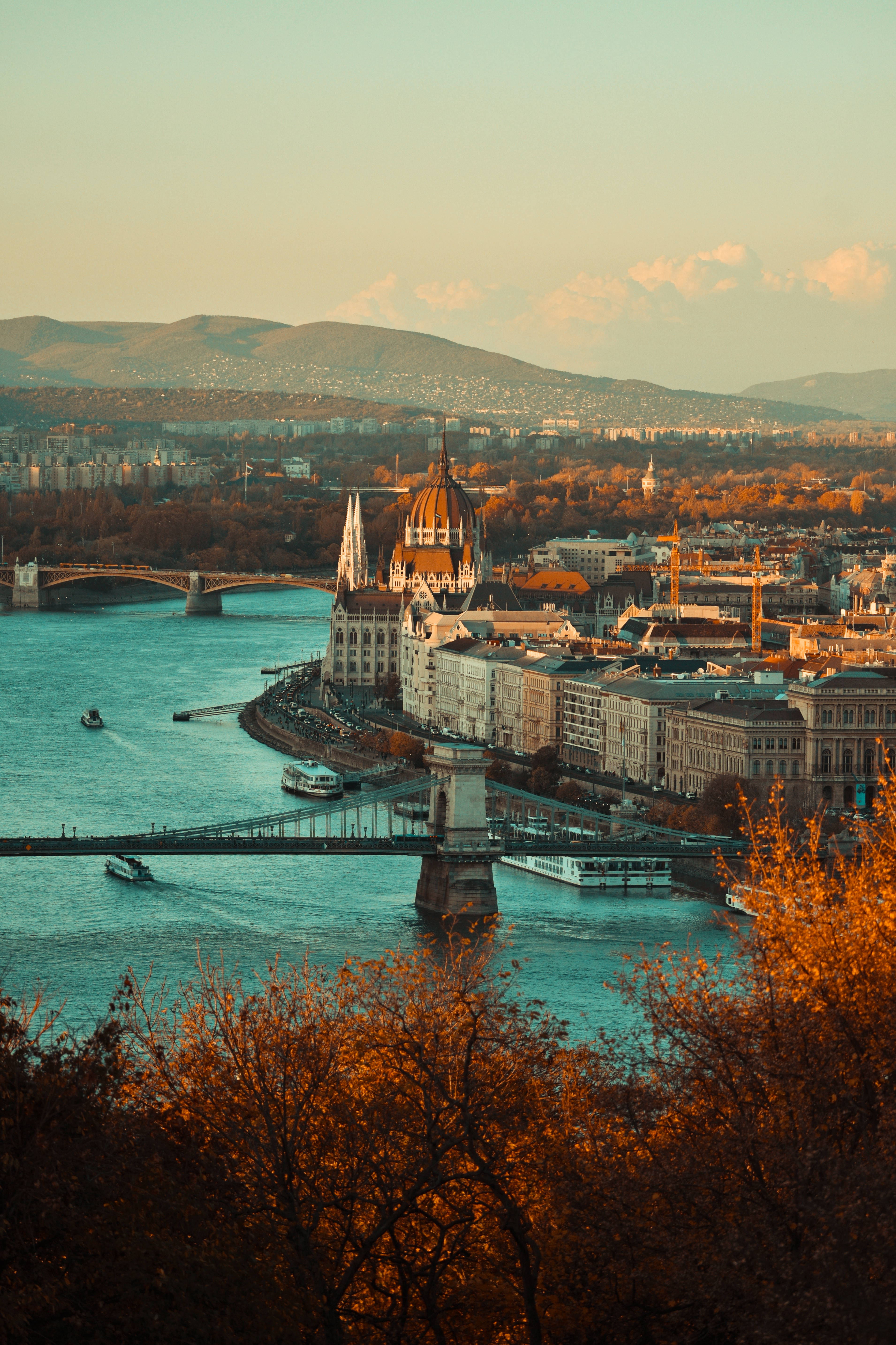 Hungary 桌布 壁紙 — 布達佩斯多瑙河黃金時段的景色，橋樑、船隻和歷史建築被秋樹環繞。