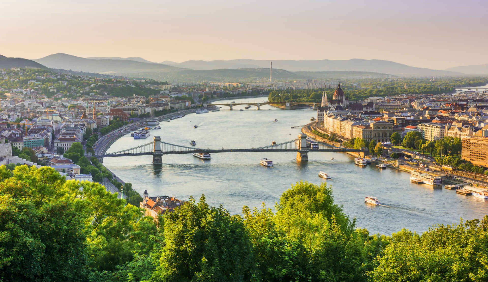 budapest 桌布 壁紙 — 布達佩斯黃金時段的全景，多瑙河流經歷史建築和前景茂密的綠樹。