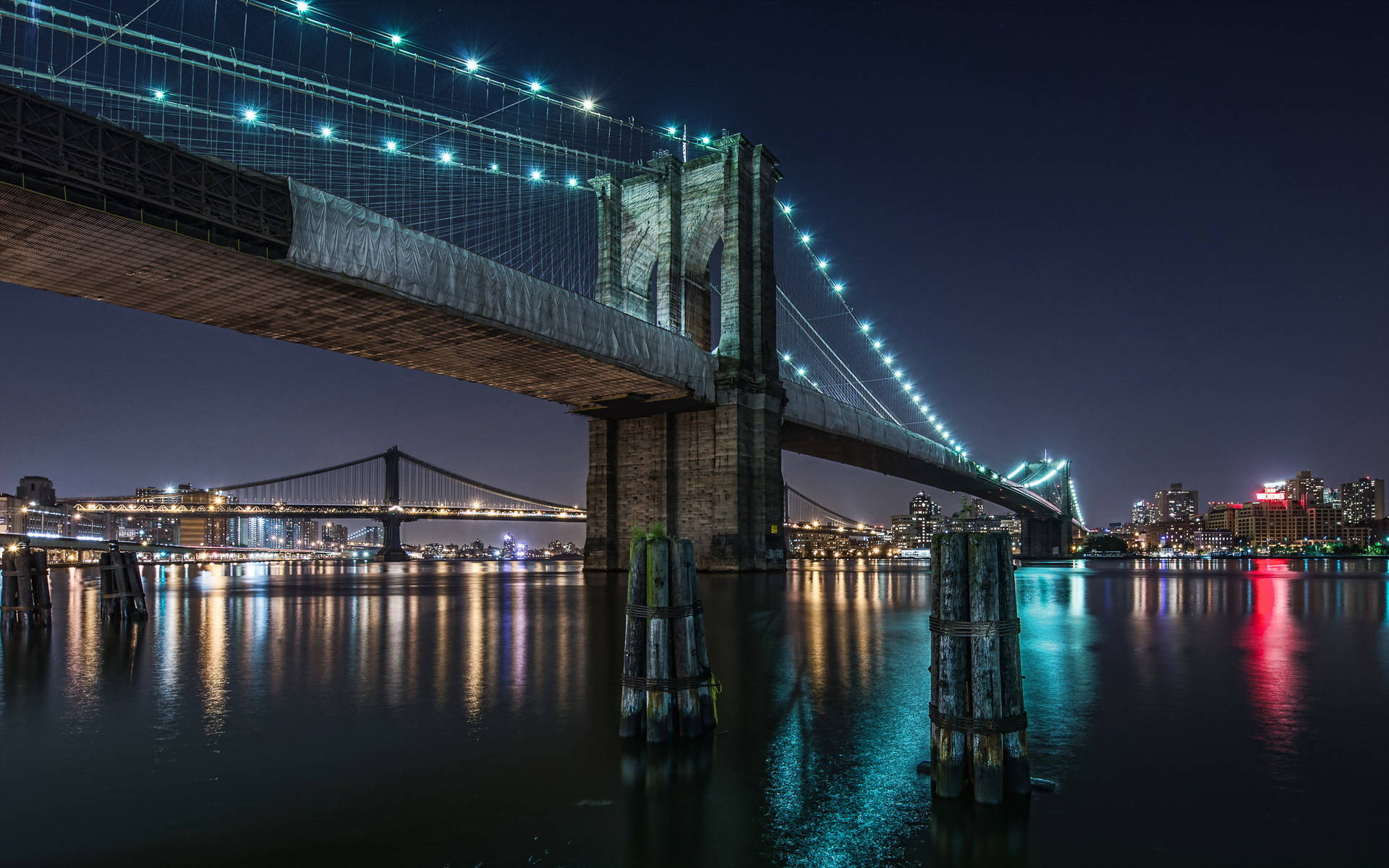 Brooklyn Bridge 桌布 壁紙 — 布魯克林大橋在夜間被發光的燈光照亮，倒映在下方平靜的水面上。