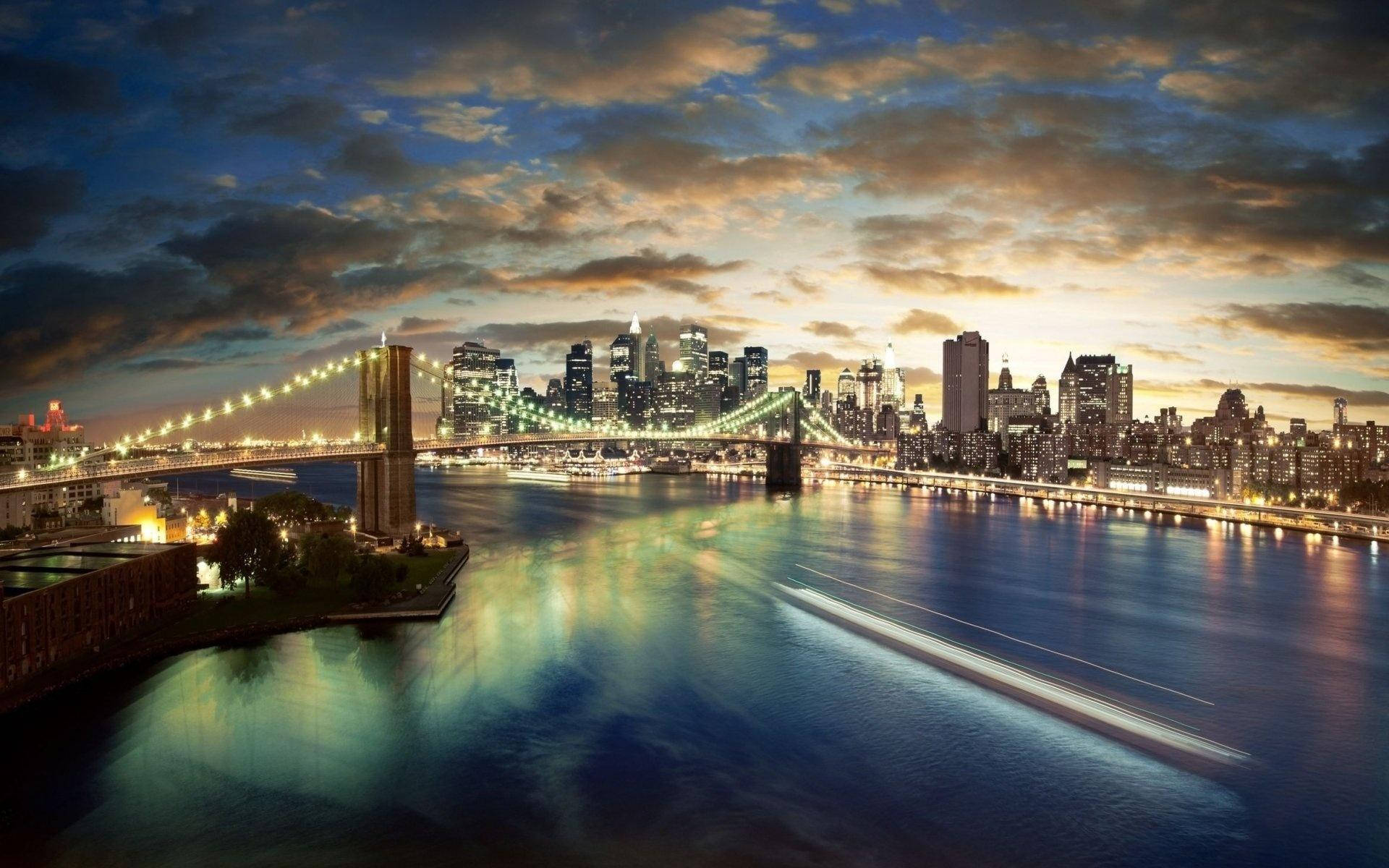 manhattan 桌布 壁紙 — 布魯克林大橋在戲劇性的暮色天空下，於倒映城市燈光的河面上閃耀著金色光芒。