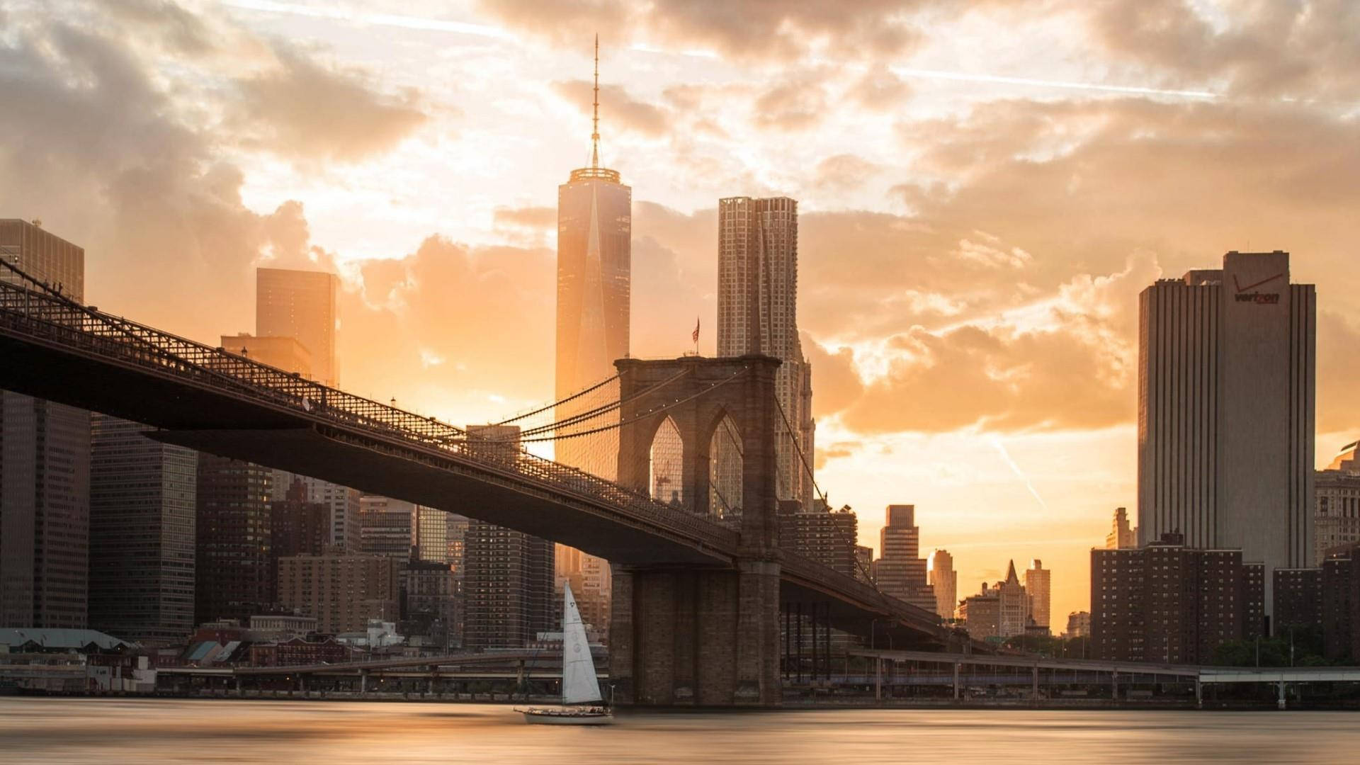 New York 桌布 壁紙 — 布魯克林大橋在金色夕陽下橫跨河流，一艘帆船在曼哈頓高聳的摩天大樓下滑行。