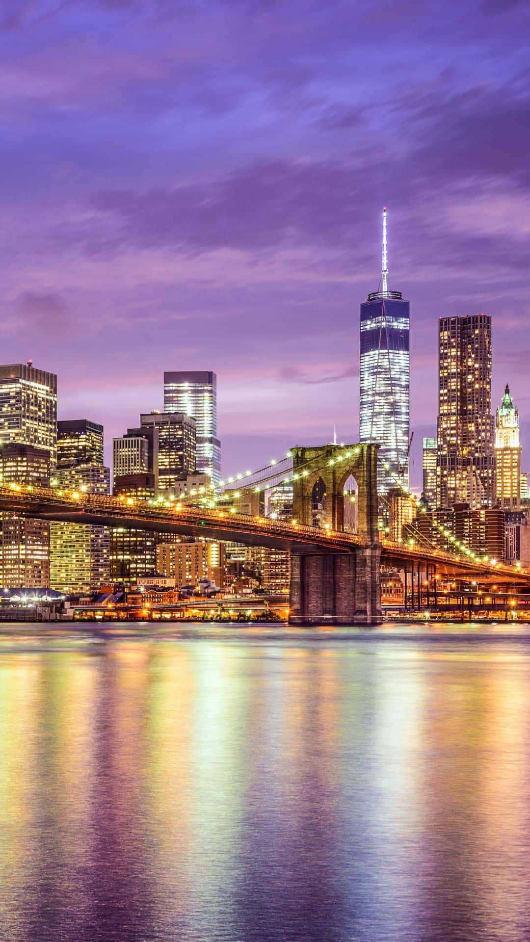 iPhone Xs New York 桌布 壁紙 — 布魯克林大橋橫跨平靜的河流，反射出金色的城市燈光，映襯著充滿活力的紫色暮色天空。
