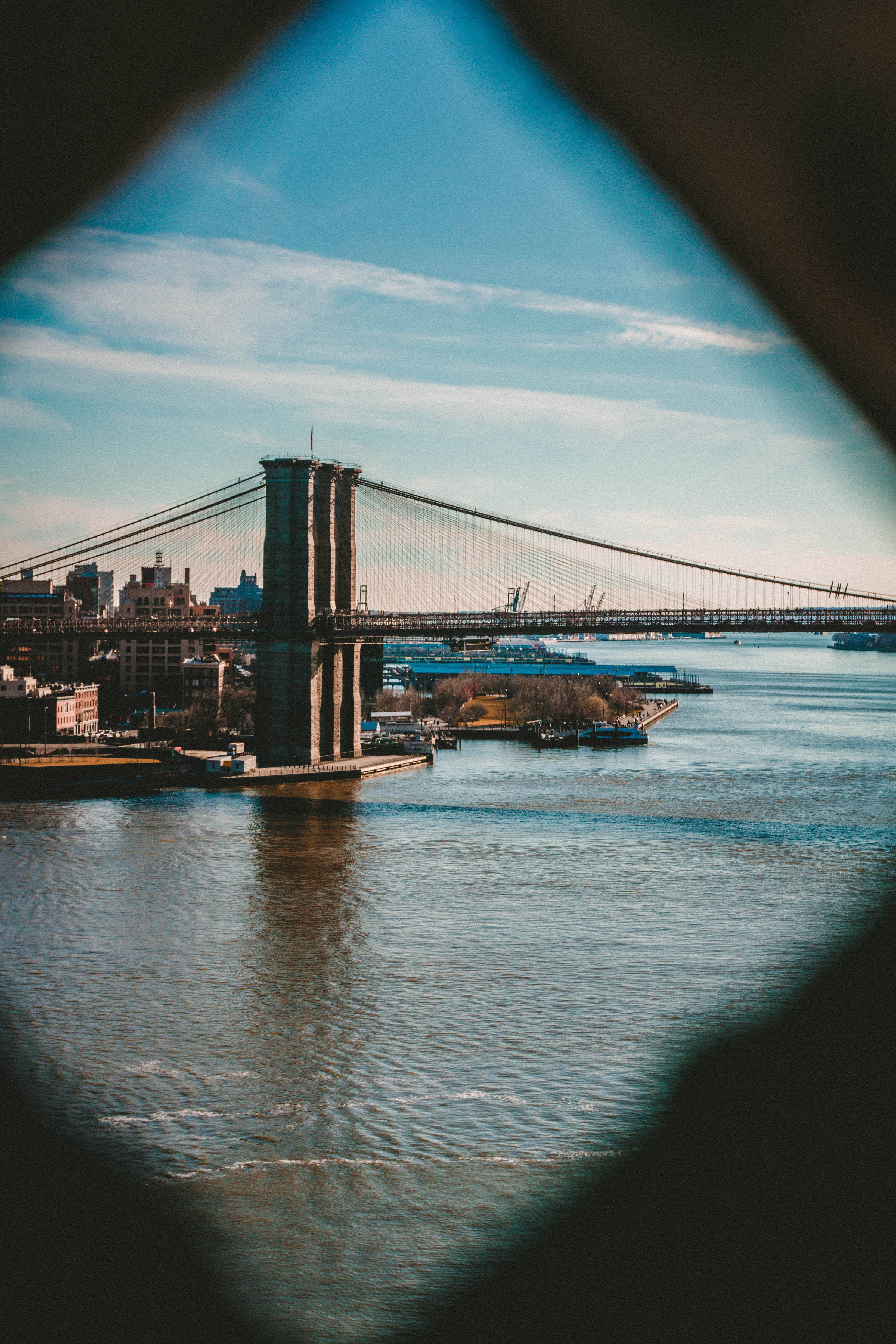 New York 桌布 壁紙 — 布魯克林大橋橫跨東河，在晴朗的藍天下透過深色圓形框架觀看。