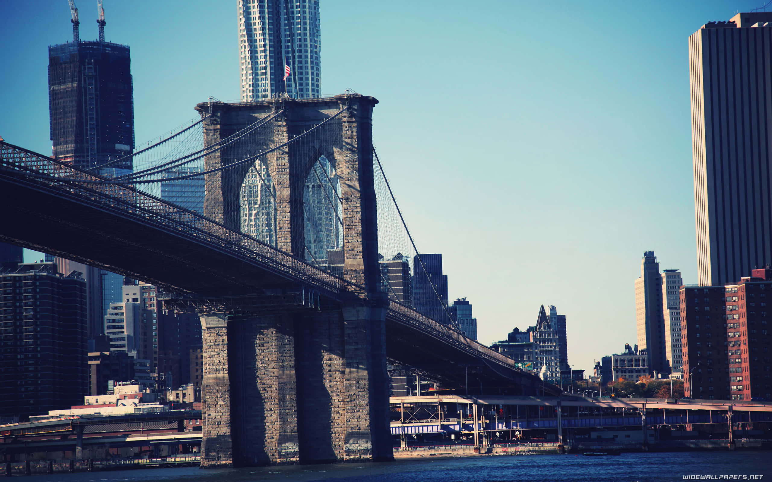 New York City 4K Ultra HD 桌布 壁紙 — 布魯克林大橋橫跨河流，背後摩天大樓在清澈藍天下聳立。