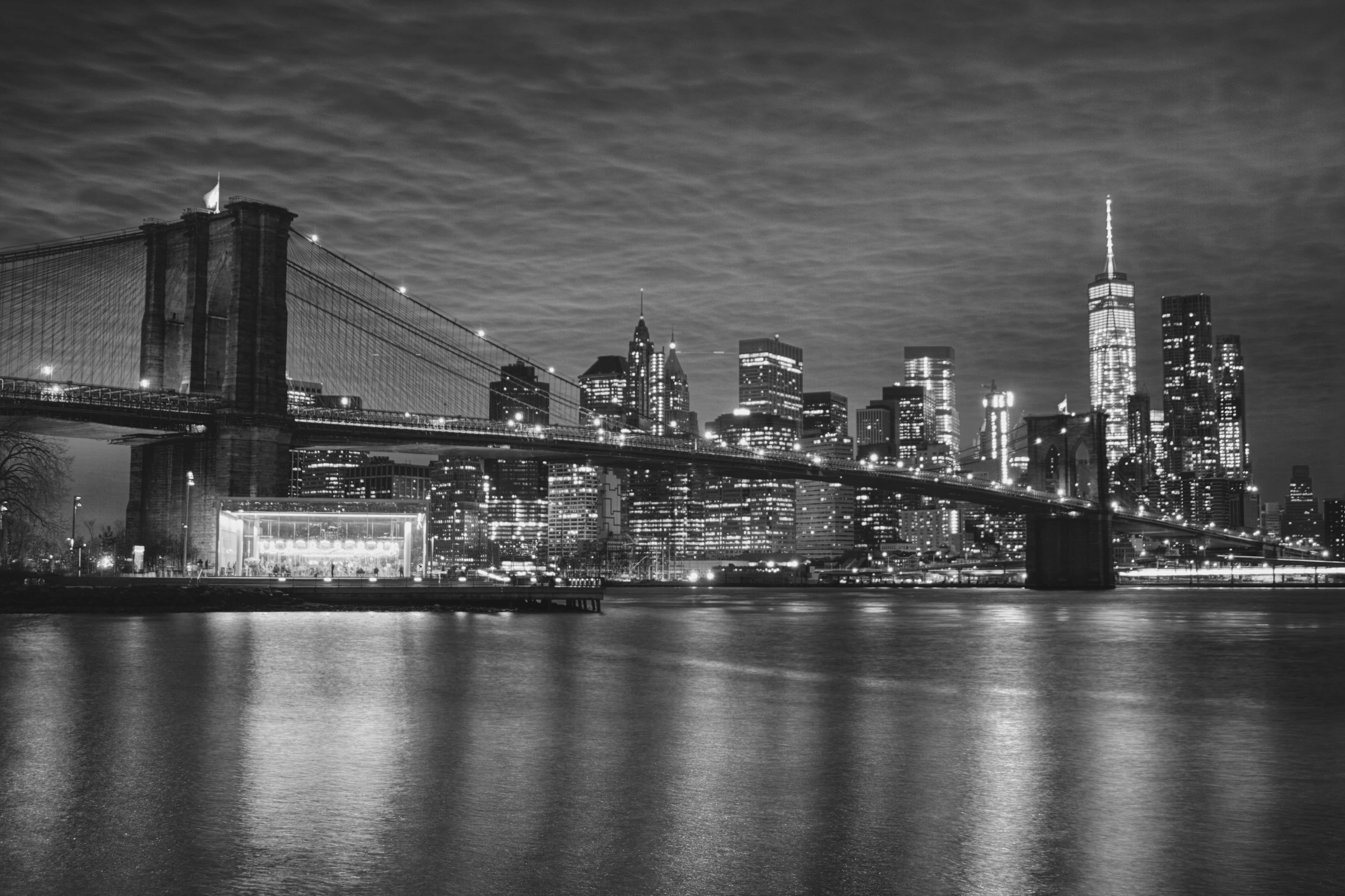 Black And White City 桌布 壁紙 — 布魯克林大橋橫跨河流的黑白夜景，背景是燈火通明的曼哈頓天際線。