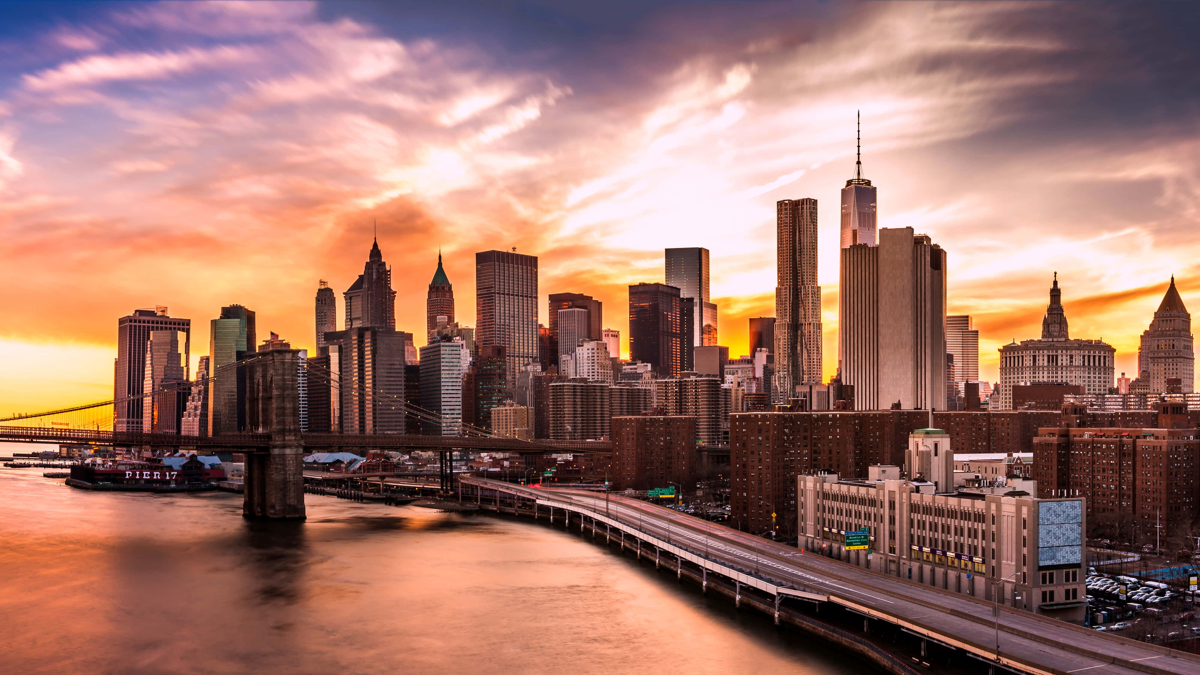 New York Skyline 桌布 壁紙 — 布魯克林大橋橫跨發光的河流，下方是曼哈頓高聳的天際線，上方是熾熱的日落天空。
