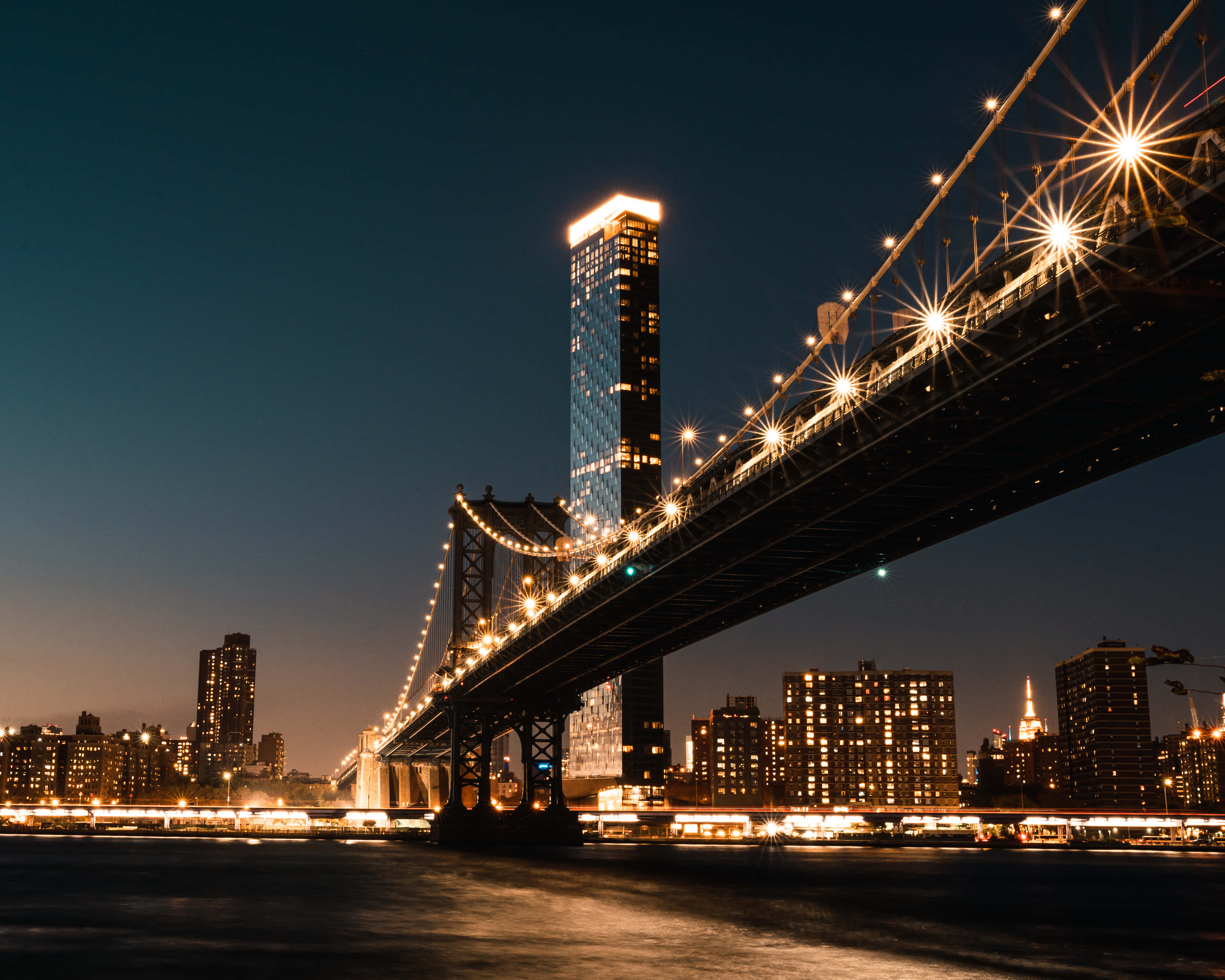 lights 桌布 壁紙 — 布魯克林大橋的壯麗夜景，燈光閃爍，映襯著深藍色的天空和城市天際線。