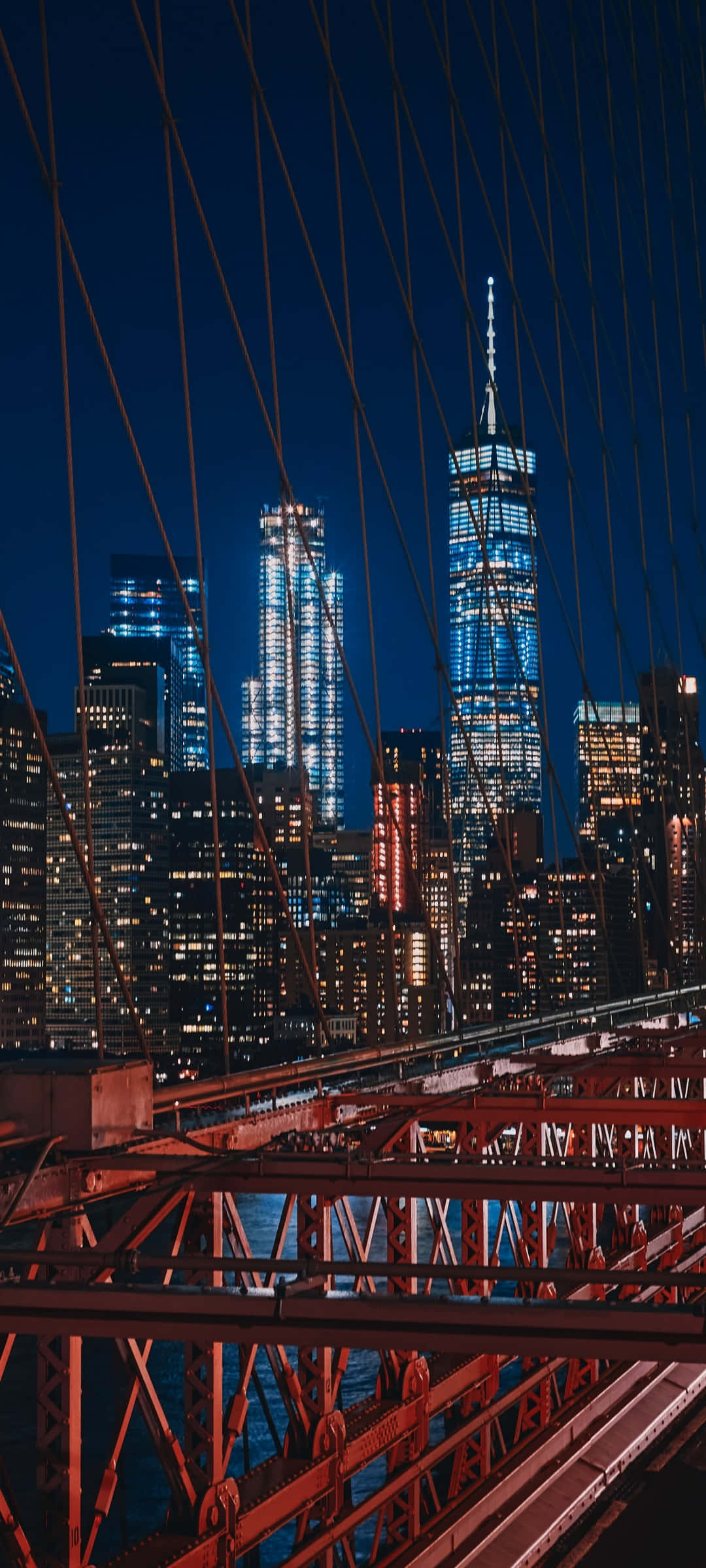 iPhone Xs New York 桌布 壁紙 — 布魯克林大橋的夜景，以藍色和紅色燈光勾勒出曼哈頓的摩天大樓。