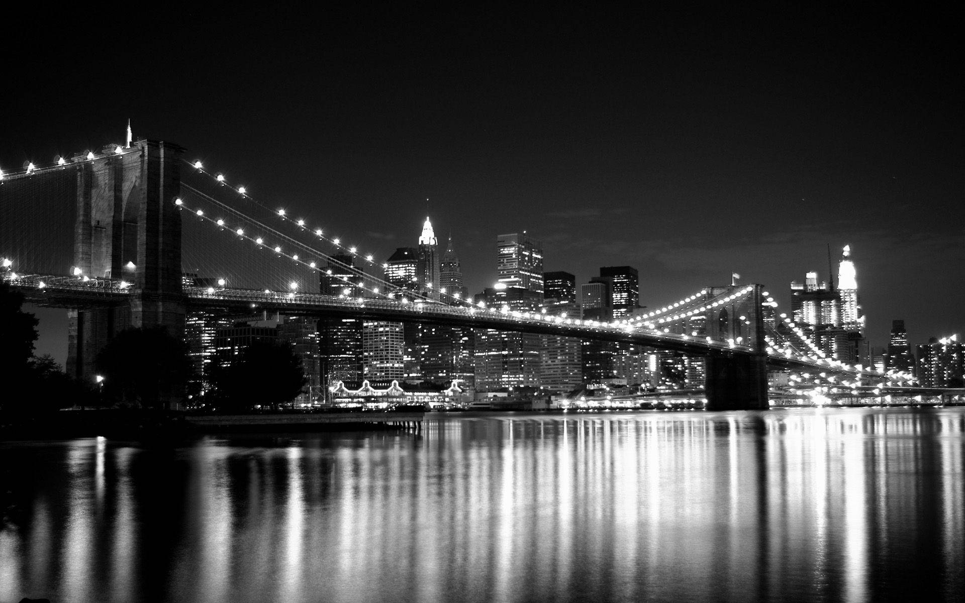 New York 桌布 壁紙 — 布魯克林大橋的醒目黑白夜景，城市燈光倒映在平靜的水面上。