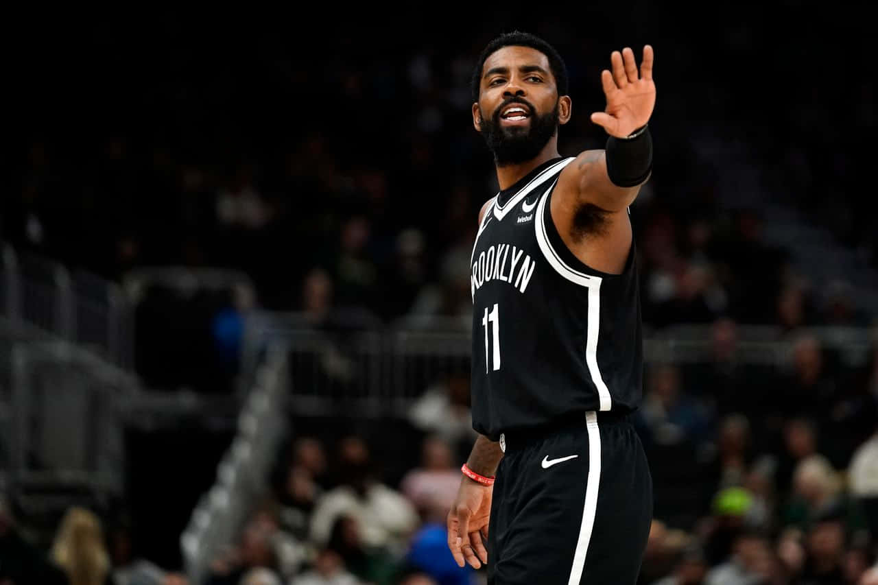 Kyrie Irving Nets 桌布 壁紙 — 布魯克林籃網球員凱里·歐文在體育館燈光下的一場籃球比賽中向球迷揮手。