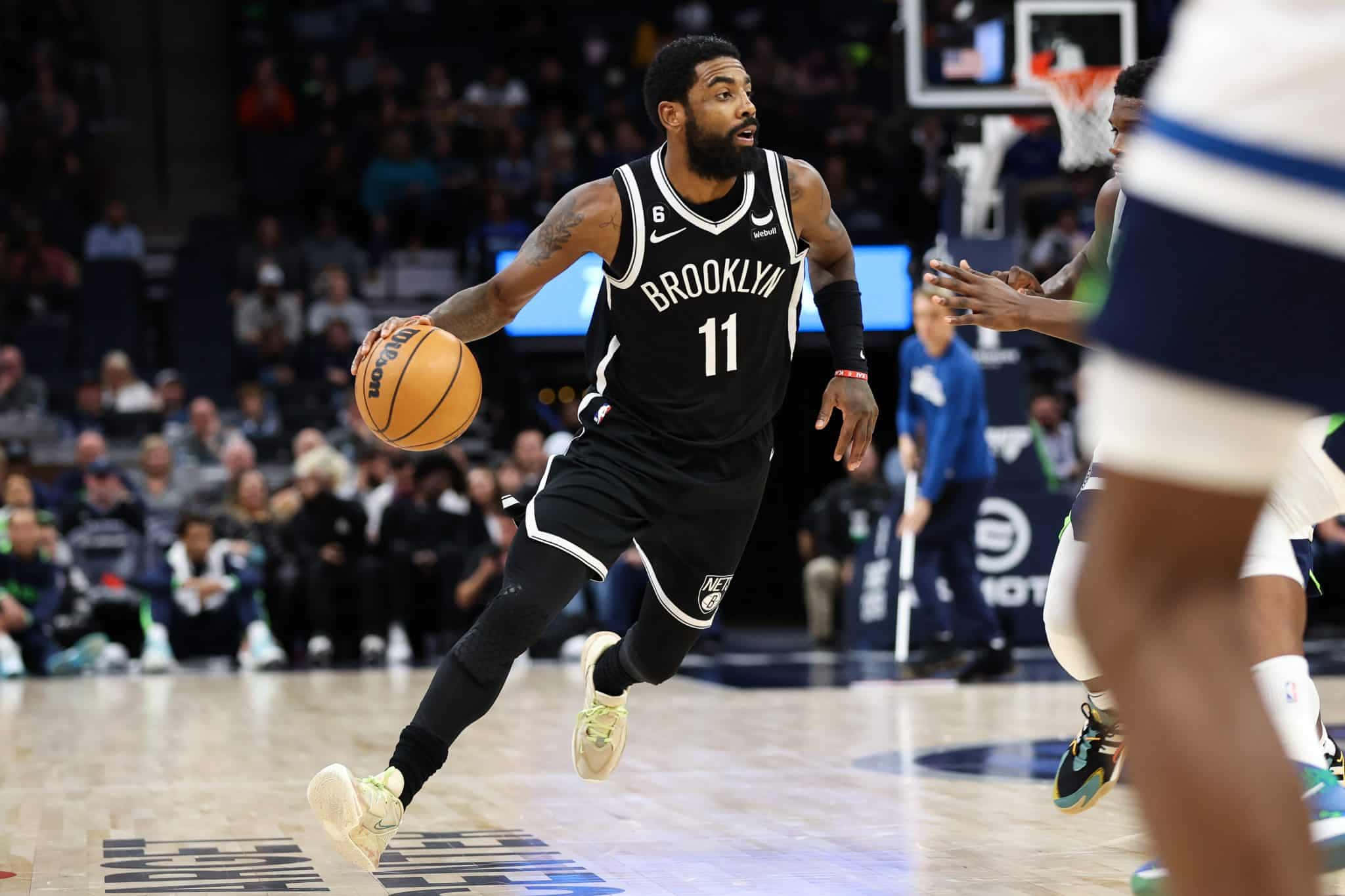 Kyrie Irving Nets 桌布 壁紙 — 布魯克林籃網球員在場館燈光下，於一場高能量的NBA比賽中積極帶球進攻。