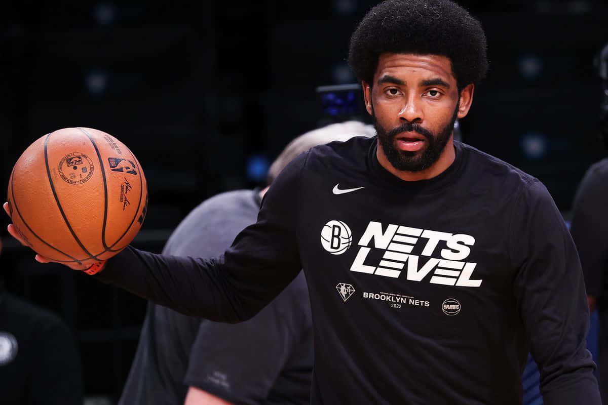 Kyrie Irving Nets 桌布 壁紙 — 布魯克林籃網球員在昏暗的球場上專注地拿著籃球。