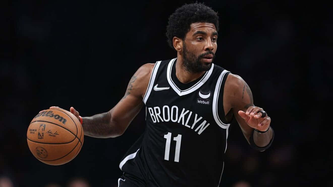 Kyrie Irving Nets 桌布 壁紙 — 布魯克林籃網隊11號球員在明亮的場館燈光下，於夜間比賽中專注地運球。