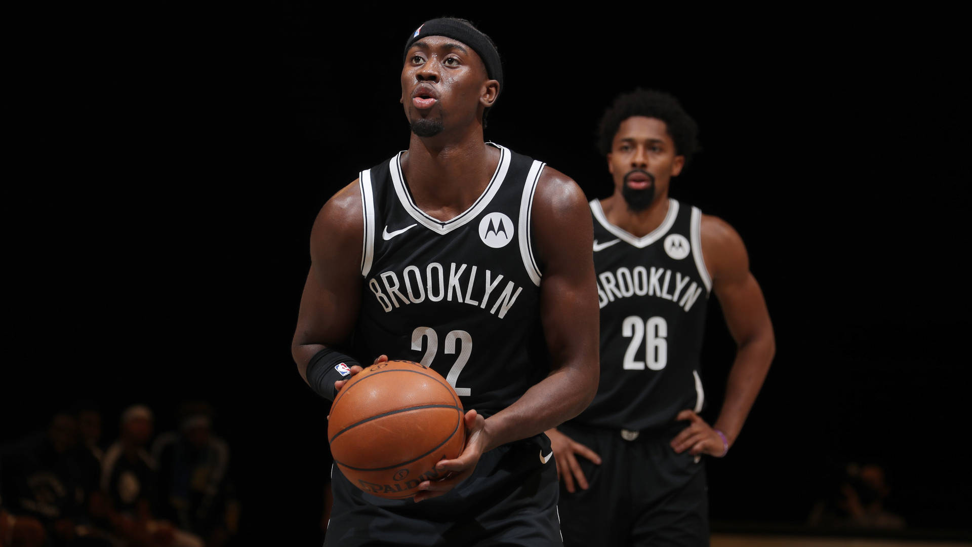 caris levert 桌布 壁紙 — 布魯克林籃網隊22號籃球運動員在球場燈光下激烈運球，隊友26號在旁密切注視。