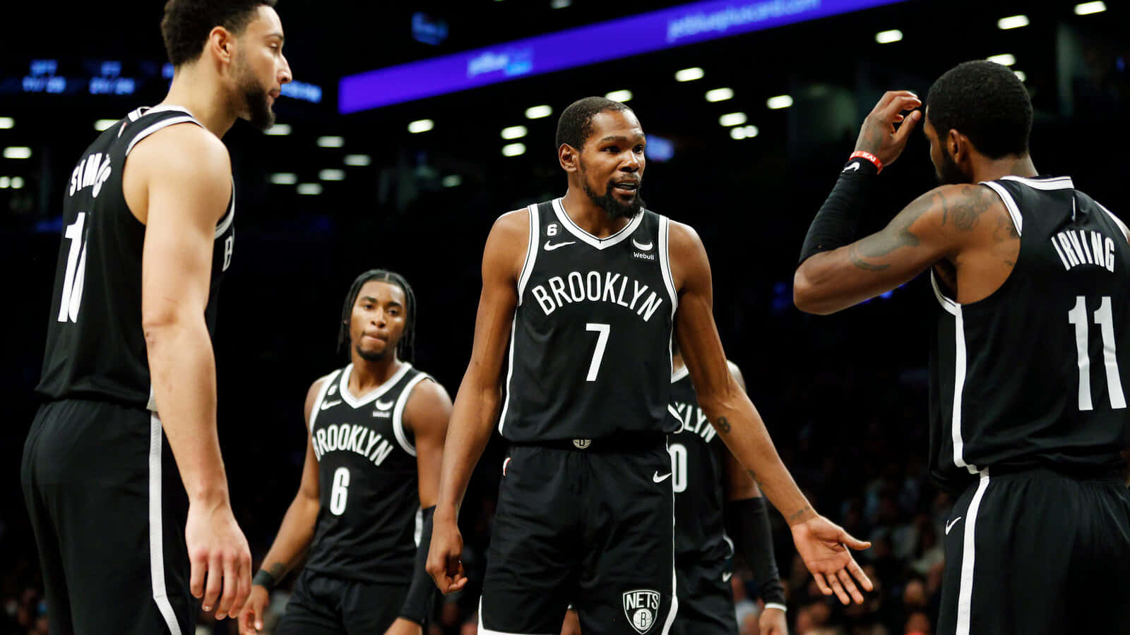Brooklyn Nets 桌布 壁紙 — 布魯克林籃網隊的籃球運動員身穿黑色球衣，在明亮的場館燈光下於比賽中激烈地圍在一起。