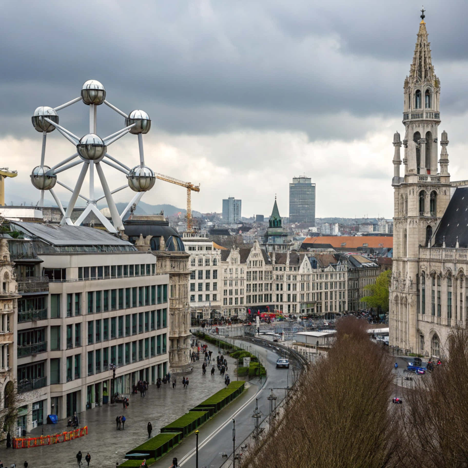Brussels skyline 壁紙 — 布魯塞爾的全景，顯示原子球塔和歷史悠久的市政廳，在陰天之下，濕漉漉的街道上有行人和汽車。