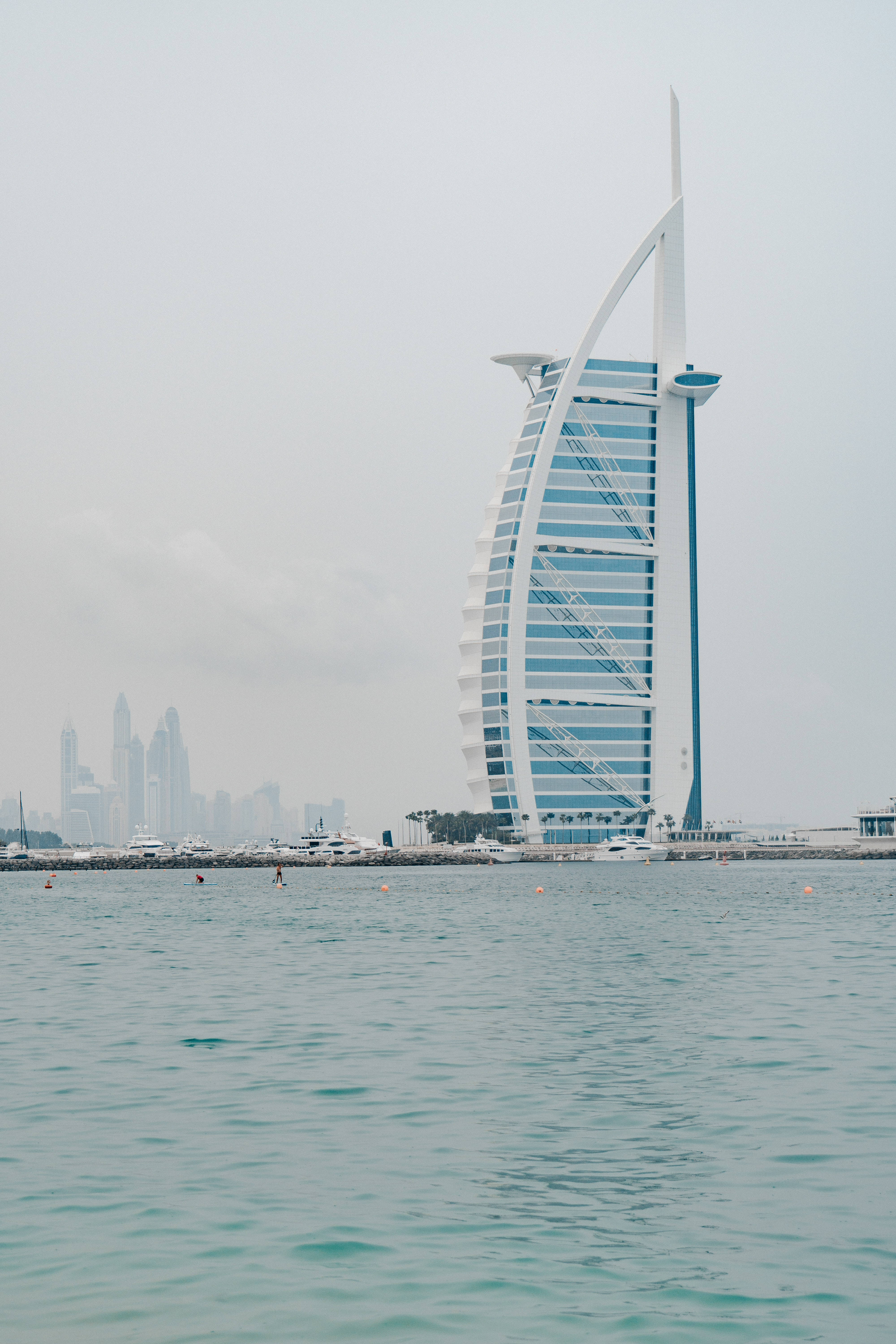 手機 桌布 壁紙 — 帆船形狀的帆船酒店（Burj Al Arab Jumeirah）高聳在朦朧的天空下，前景是平靜的碧綠海水。