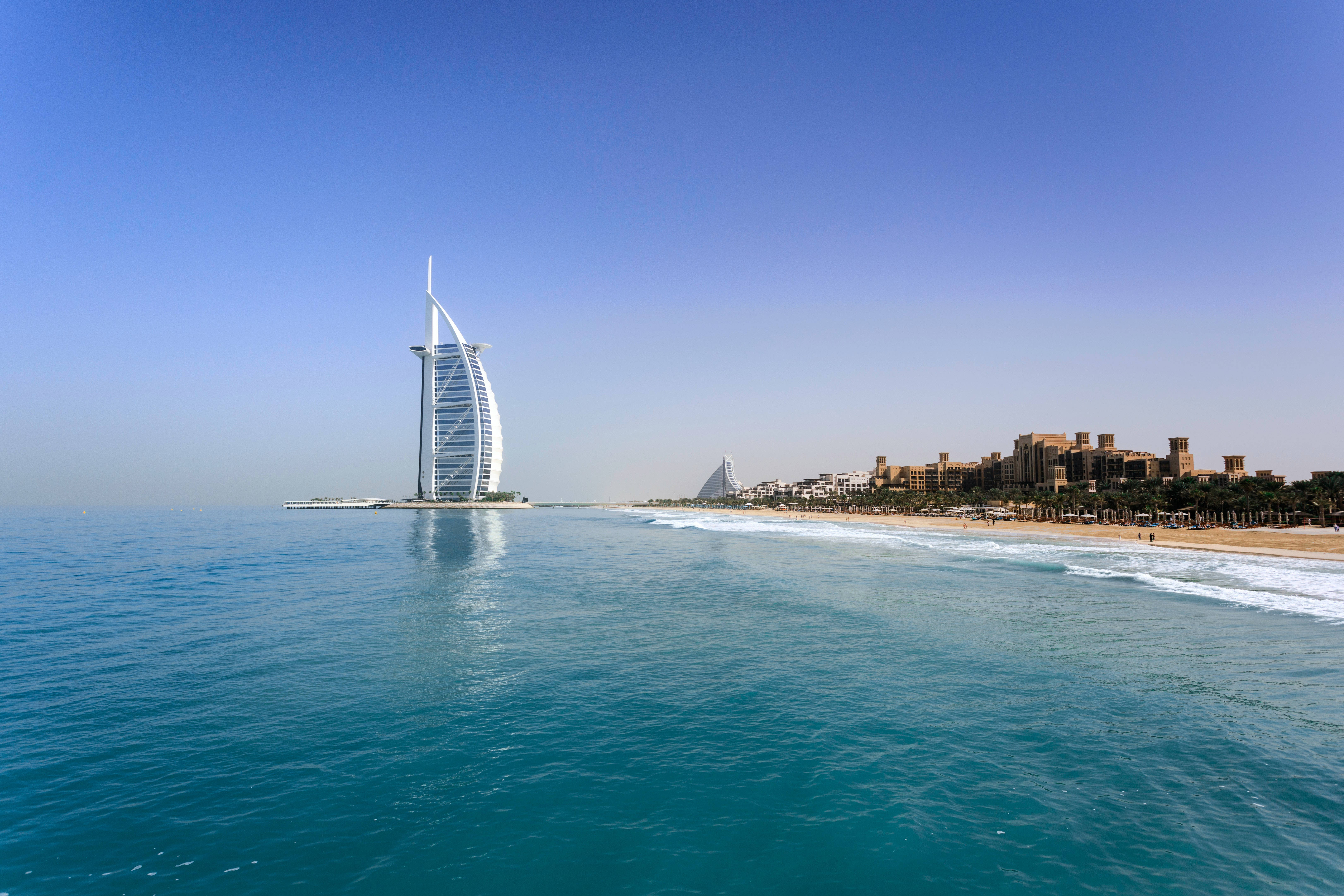 海灘 桌布 壁紙 — 帆船形狀的帆船酒店（Burj Al Arab）雄偉地矗立在沙漠島嶼上，四周是碧綠的海水，旁邊是沙灘，上方是清澈的藍天。