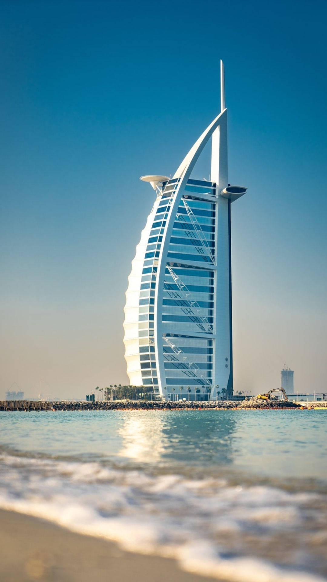 杜拜 桌布 壁紙 — 帆船形狀的帆船飯店（Burj Al Arab Jumeirah）在晴朗的藍天下閃耀，溫柔的海浪拍打著前景的海岸。