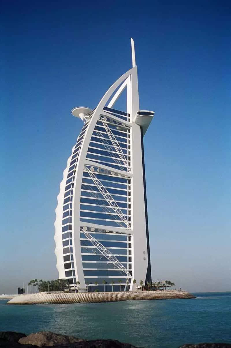建築 桌布 壁紙 — 帆船形狀的帆船飯店（Burj Al Arab Jumeirah）在清澈的藍天下高聳，白色外牆在碧綠的海水上反射陽光。