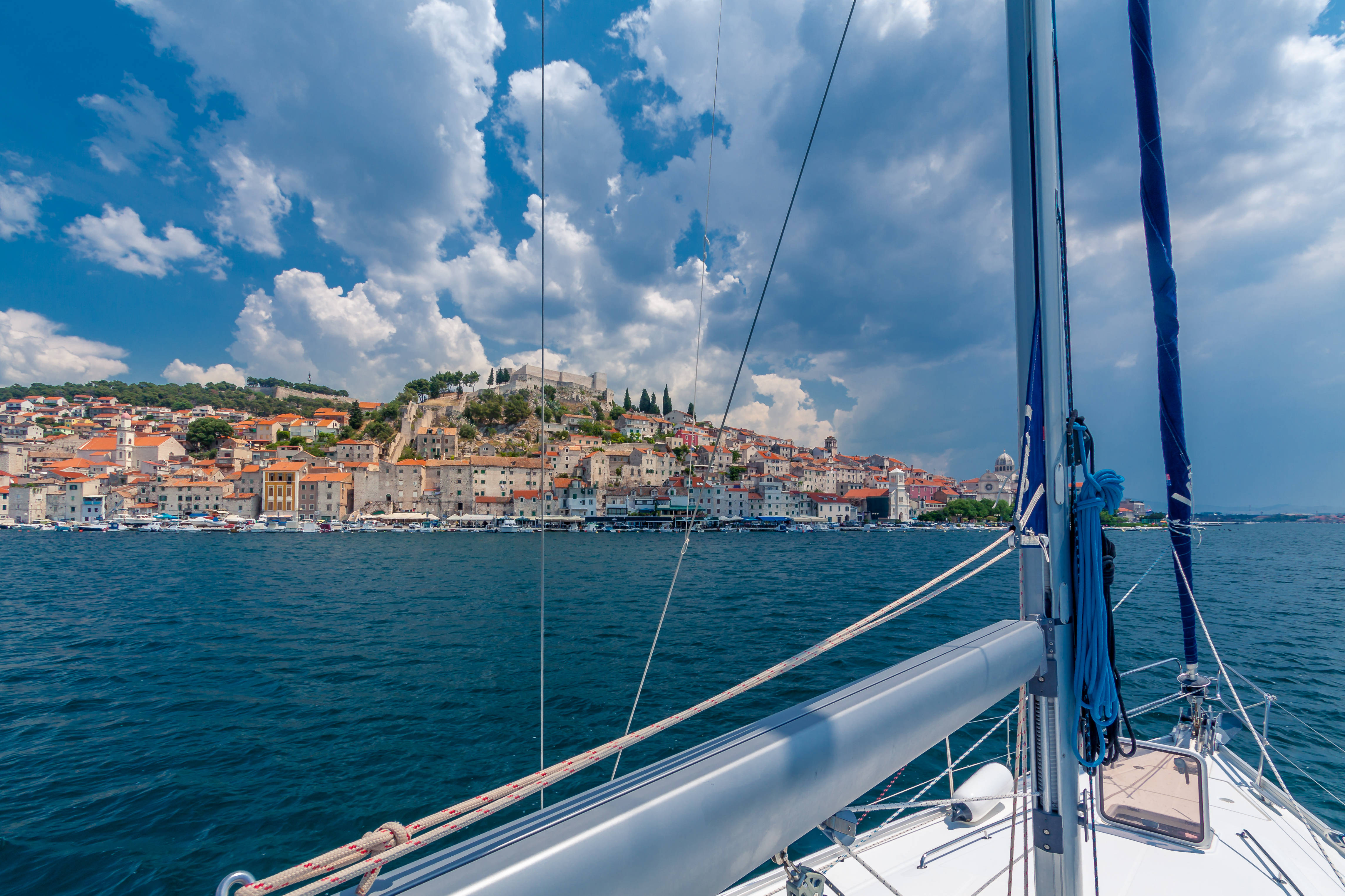 Croatia 桌布 壁紙 — 帆船景觀，海岸小鎮的陶土屋頂坐落在山坡上，在戲劇性的藍天和蓬鬆的雲朵下。
