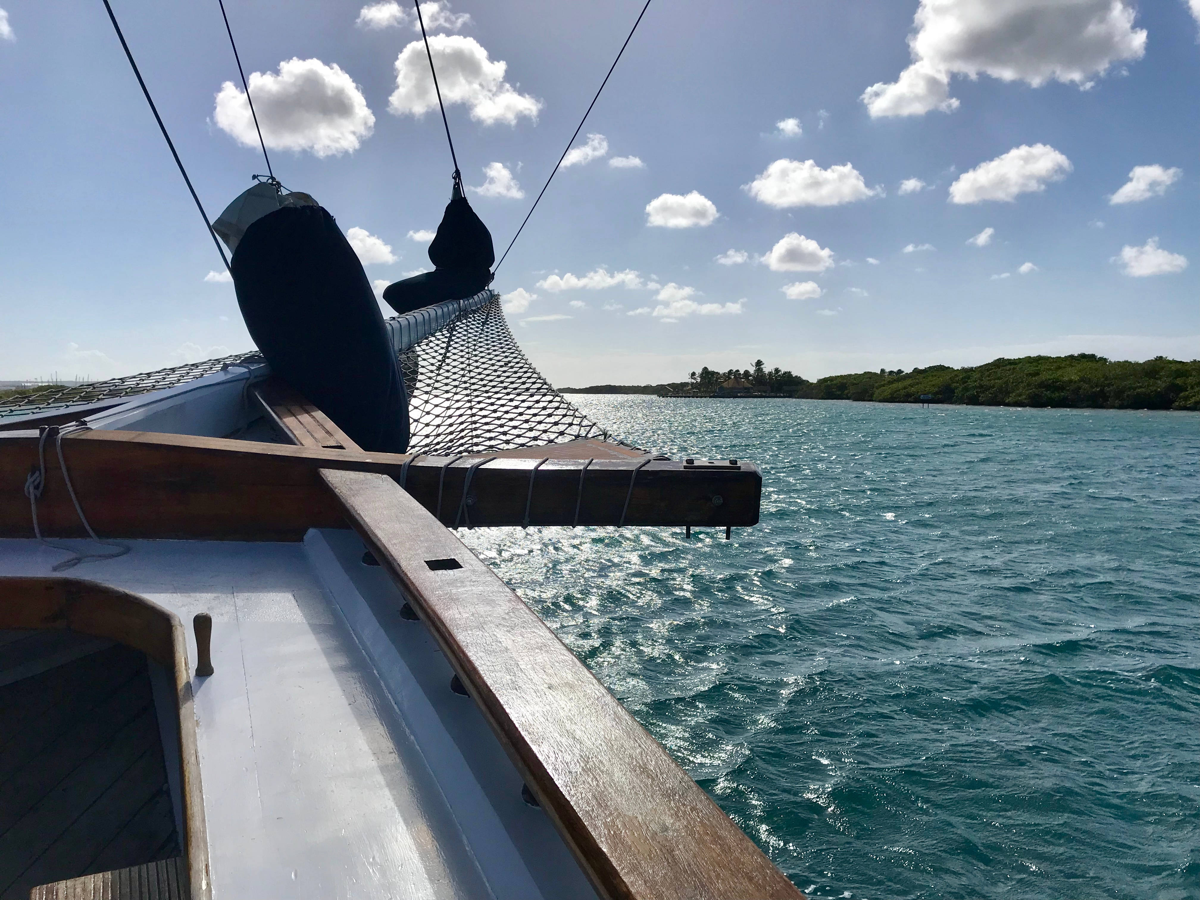 Aruba 桌布 壁紙 — 帆船的船頭在明亮的藍天下劃過碧綠的海水，天空點綴著蓬鬆的白雲。
