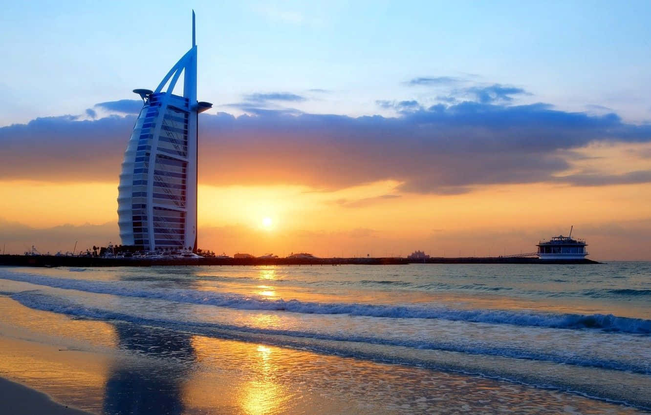 Uae 桌布 壁紙 — 帆船酒店在日落時雄偉地矗立，金色的光線反射在海浪和天空上。