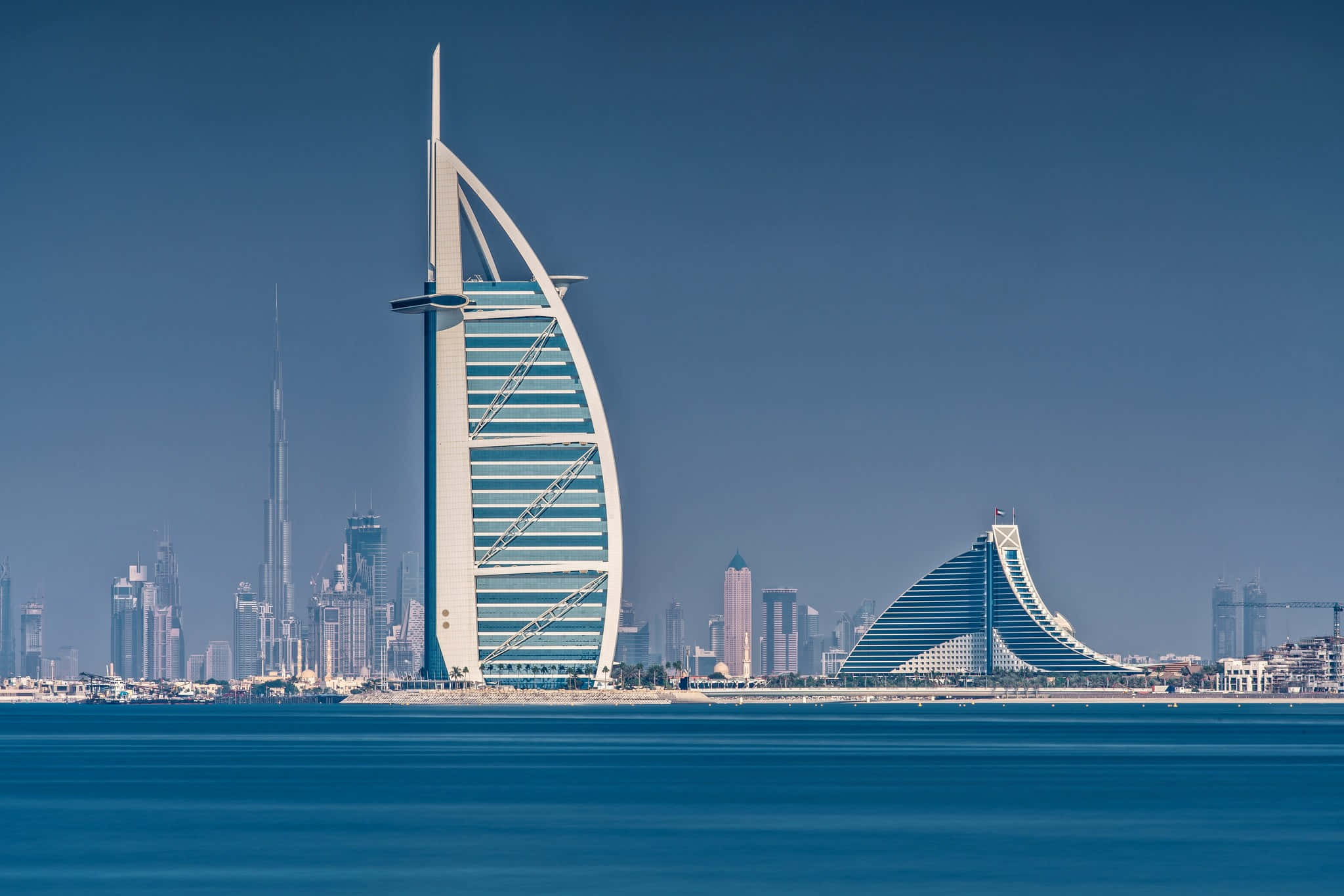Burj Khalifa 桌布 壁紙 — 帆船飯店（Burj Al Arab）矗立在清澈的藍天下，平靜的水面映照出其標誌性的帆船形狀。