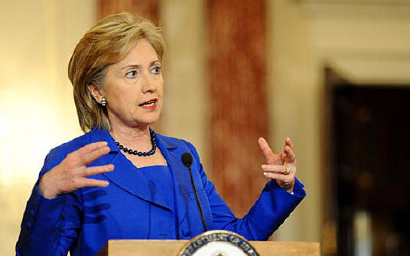 hillary clinton 桌布 壁紙 — 希拉蕊·柯林頓在正式室內場合中，身穿大膽的藍色套裝，在講台上充滿激情地發言。