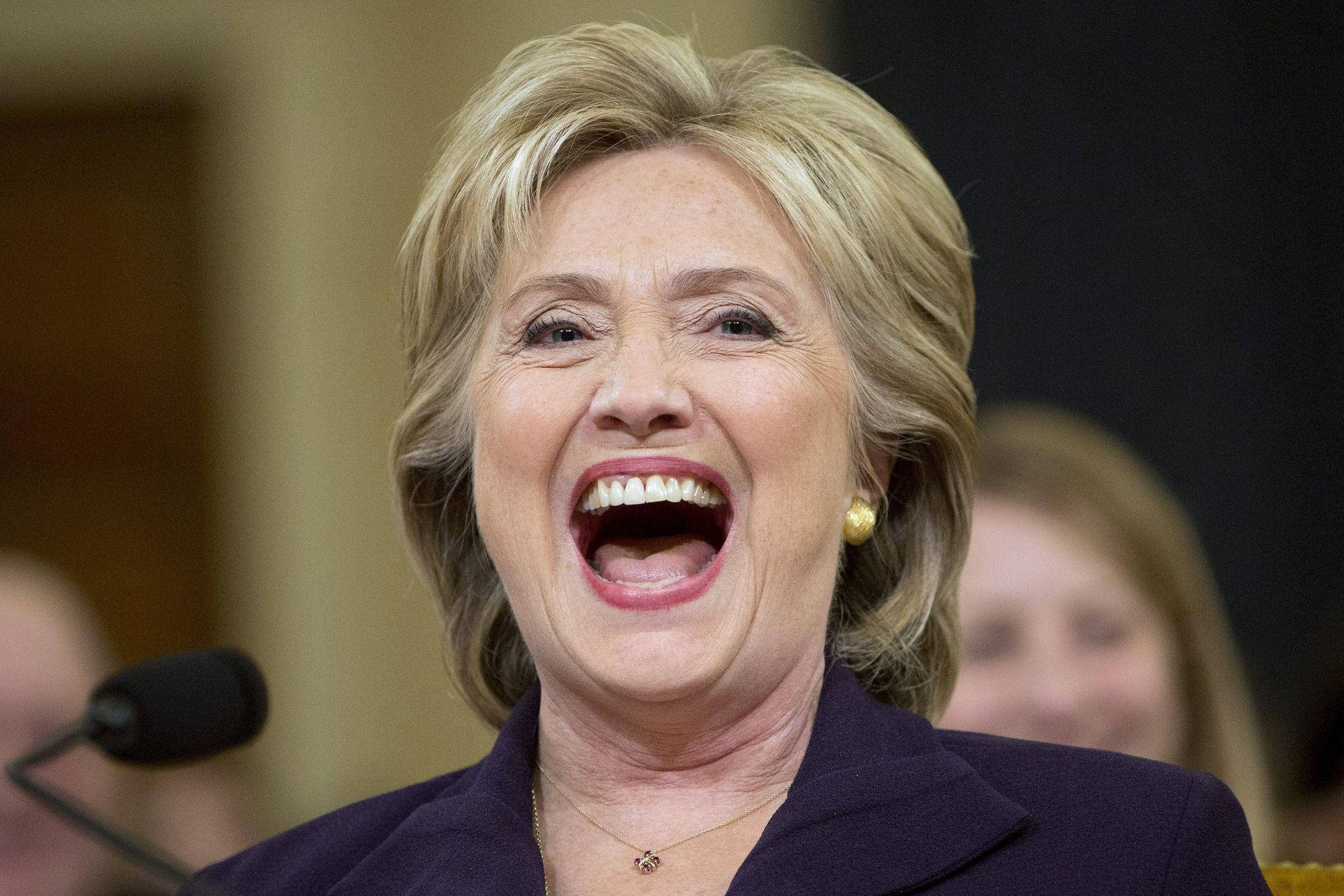 hillary clinton 桌布 壁紙 — 希拉蕊·柯林頓張開嘴大笑，露出牙齒，穿著深色西裝外套和金色耳環。