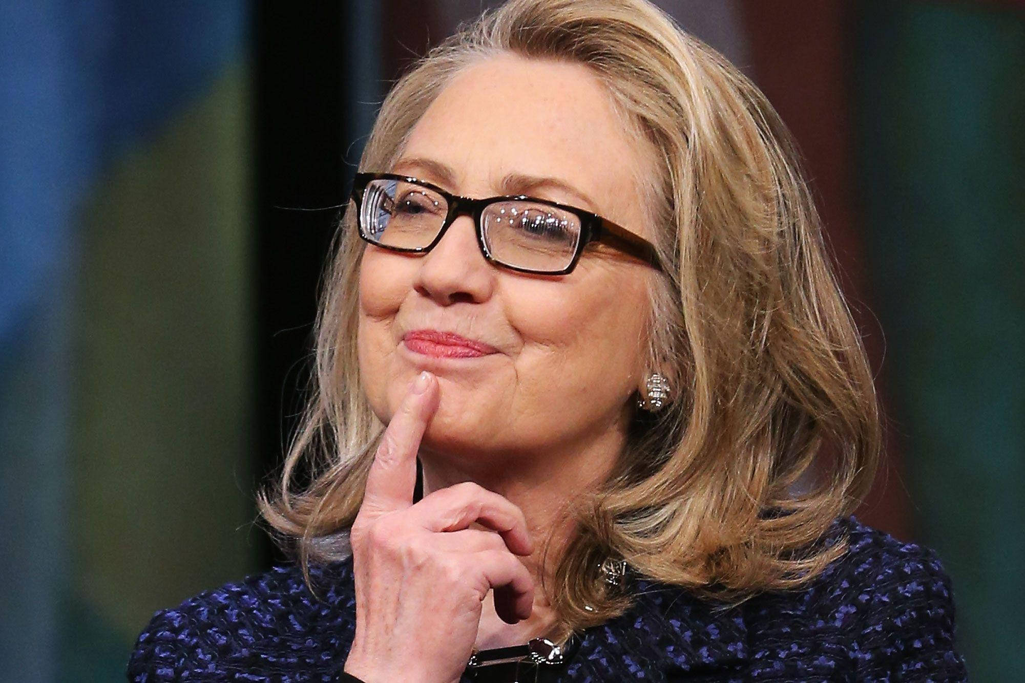 hillary clinton 桌布 壁紙 — 希拉蕊·柯林頓的近照，手指放在下巴上，戴著眼鏡和圖案西裝外套，若有所思地微笑。