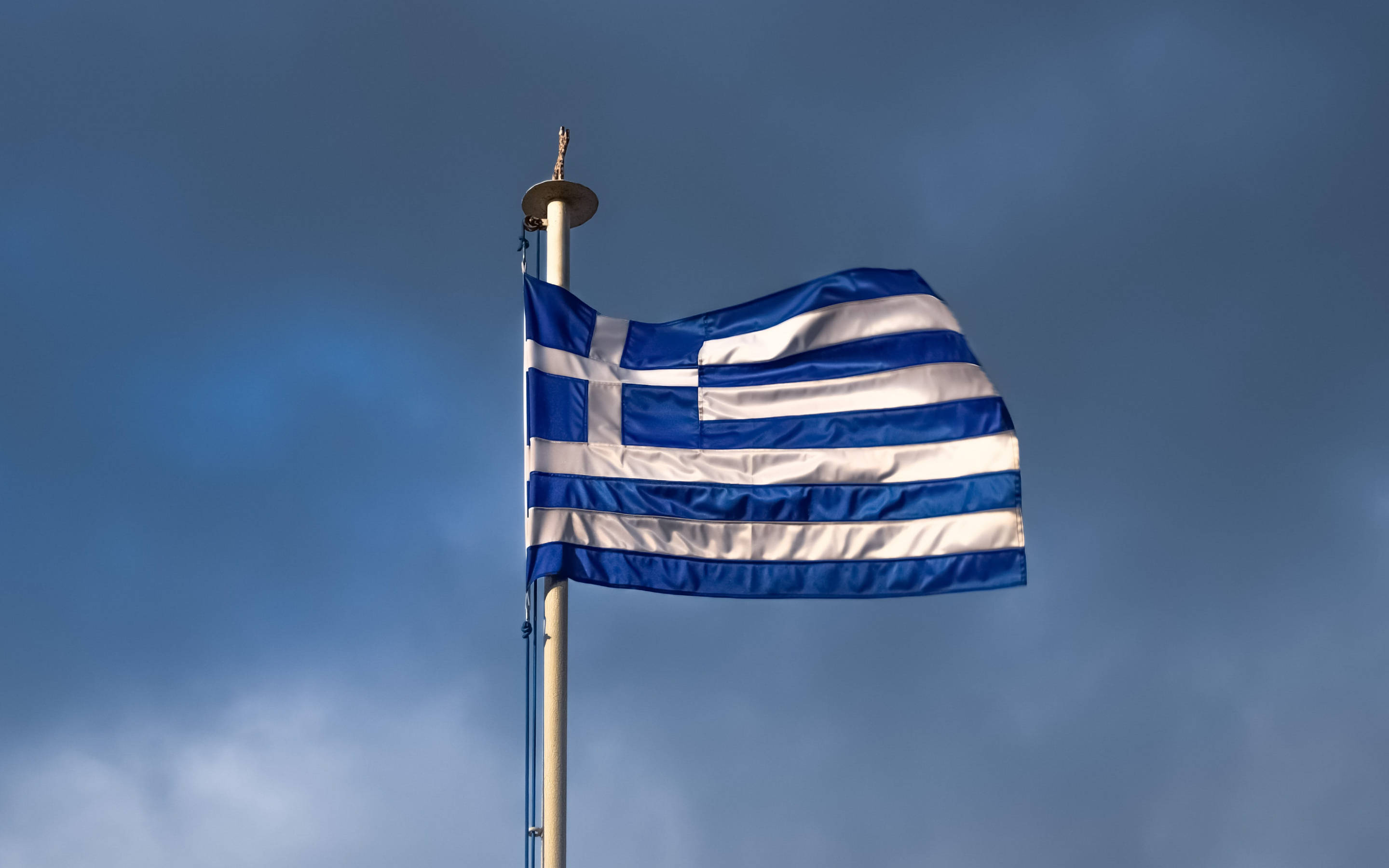 greek 桌布 壁紙 — 希臘國旗，藍白條紋和十字架，在陰沉多雲的天空中飄揚。