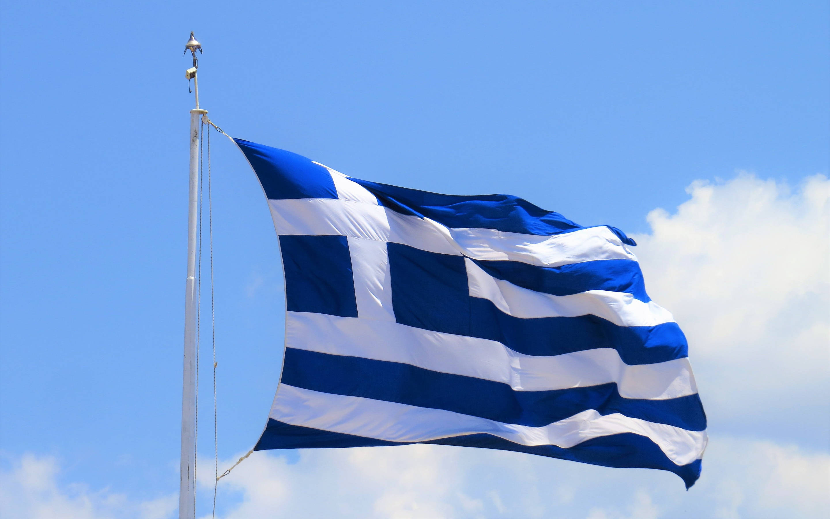 greek 桌布 壁紙 — 希臘國旗上的藍白條紋和十字架在藍天白雲中驕傲飄揚。