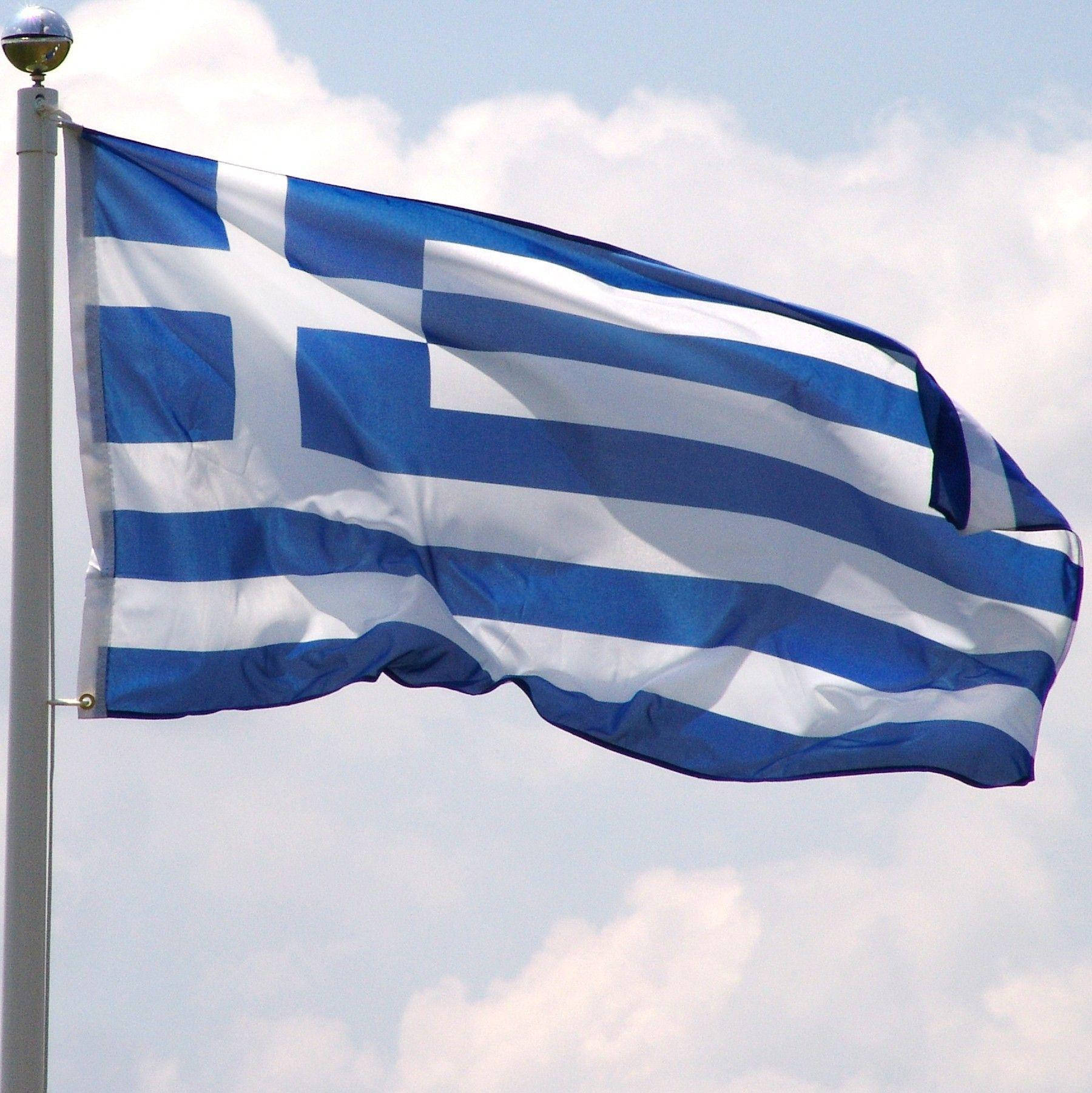 greek 桌布 壁紙 — 希臘國旗帶有藍白條紋和十字架，在部分多雲的天空下動態飄揚。