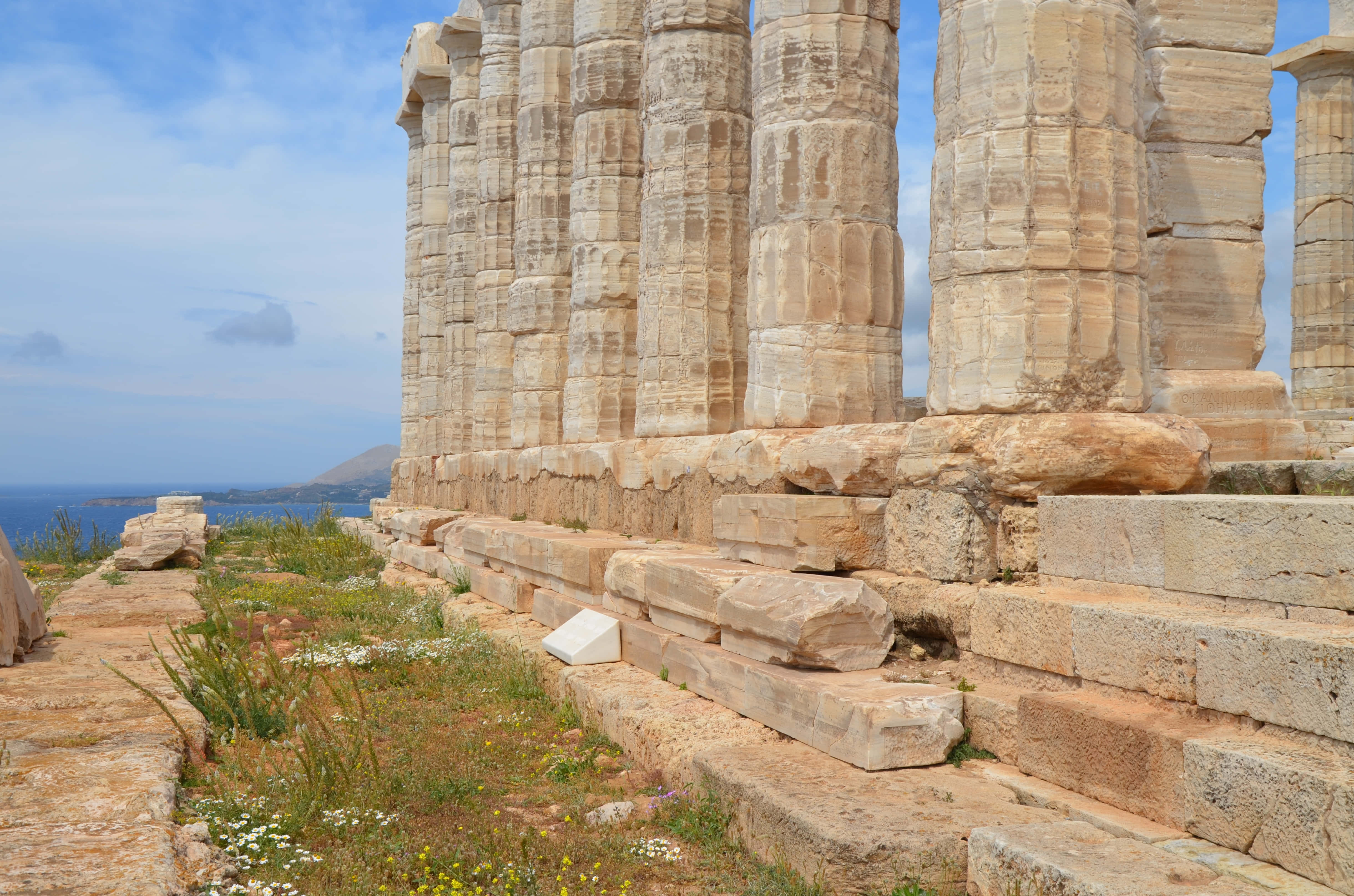 Greek Aesthetic 桌布 壁紙 — 希臘神廟的古老石柱歷經風霜，聳立在部分多雲的天空下，俯瞰著藍色的大海。