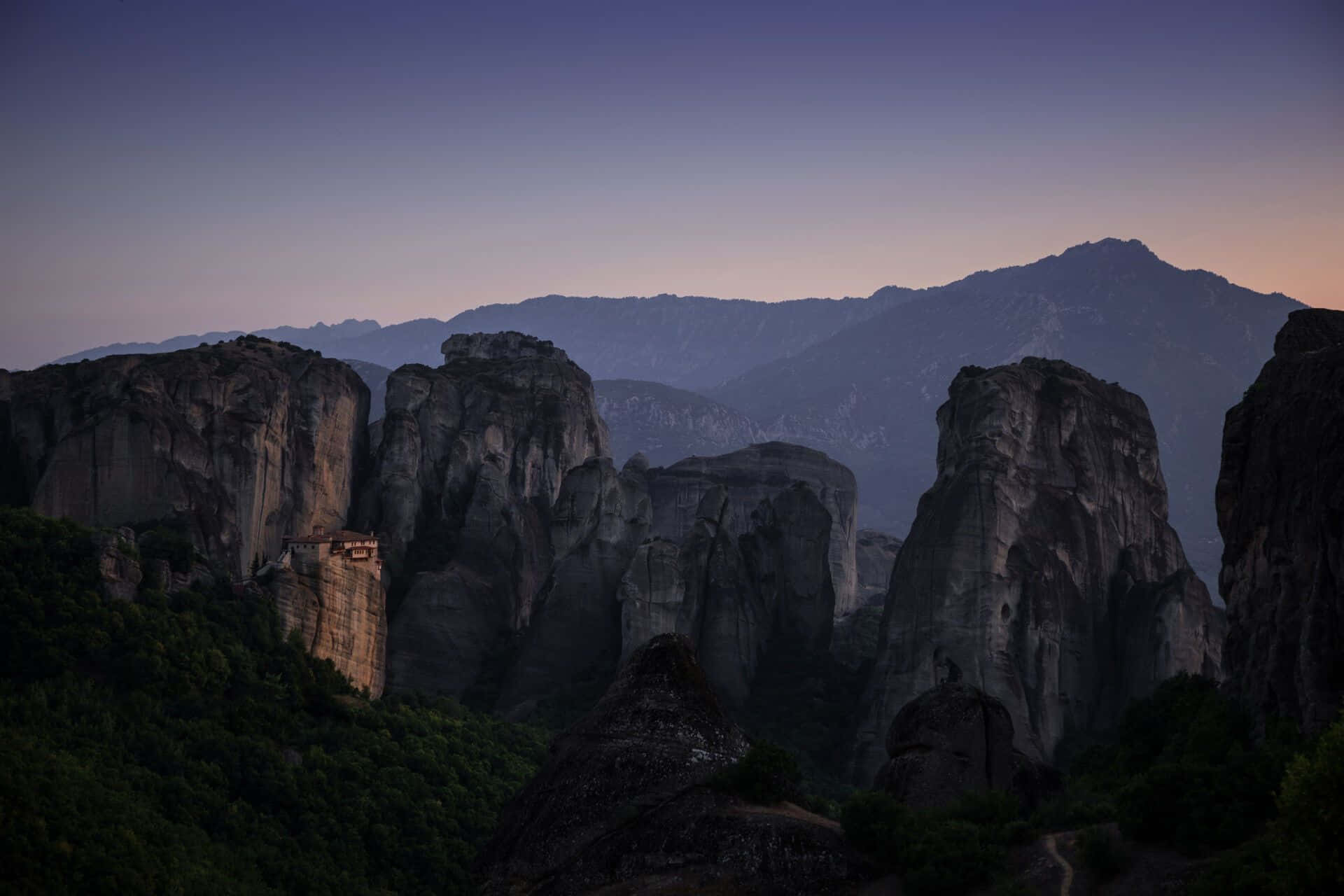 Awe-inspiring 桌布 壁紙 — 希臘邁泰奧拉的黃昏時分，古老修道院依附在 towering 岩石柱上，天空呈現紫色和橙色。
