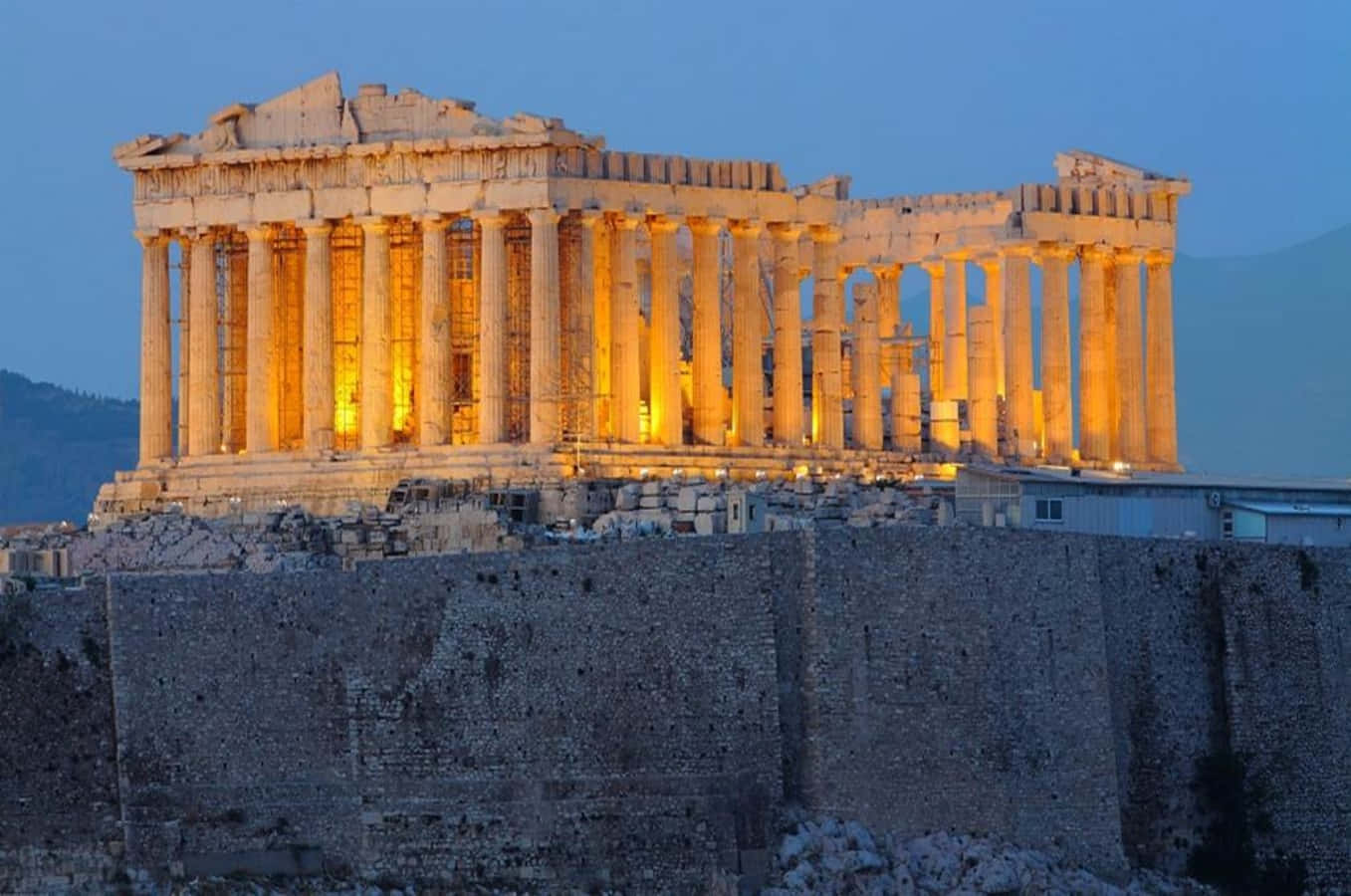 greek 桌布 壁紙 — 帕德嫩神廟在古老的山丘上，在深藍色的暮色天空下，被金色的燈光溫暖地照亮。