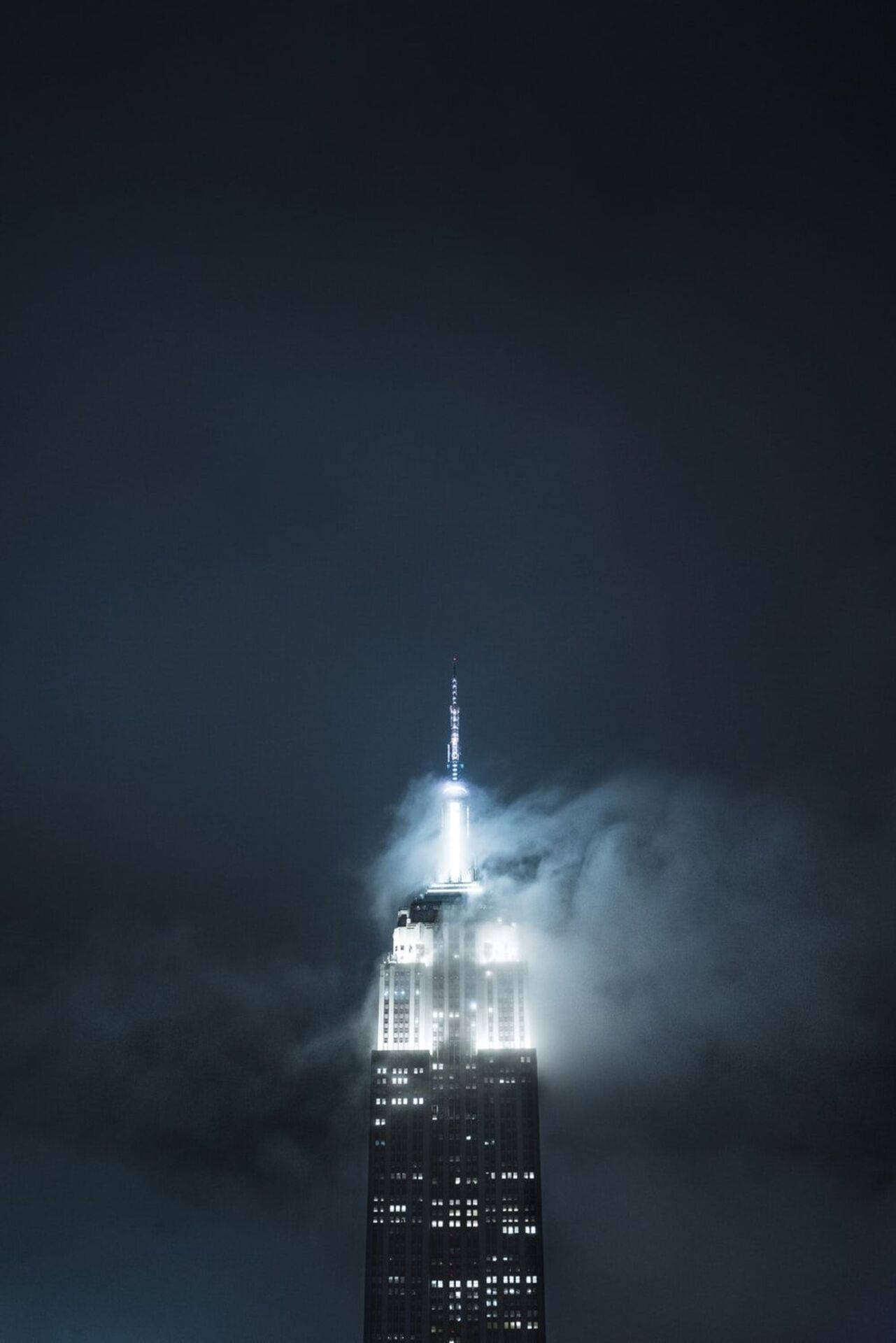 Screen 桌布 壁紙 — 帝國大廈刺穿黑暗多雲的夜空，其明亮的尖頂在薄霧中閃耀。