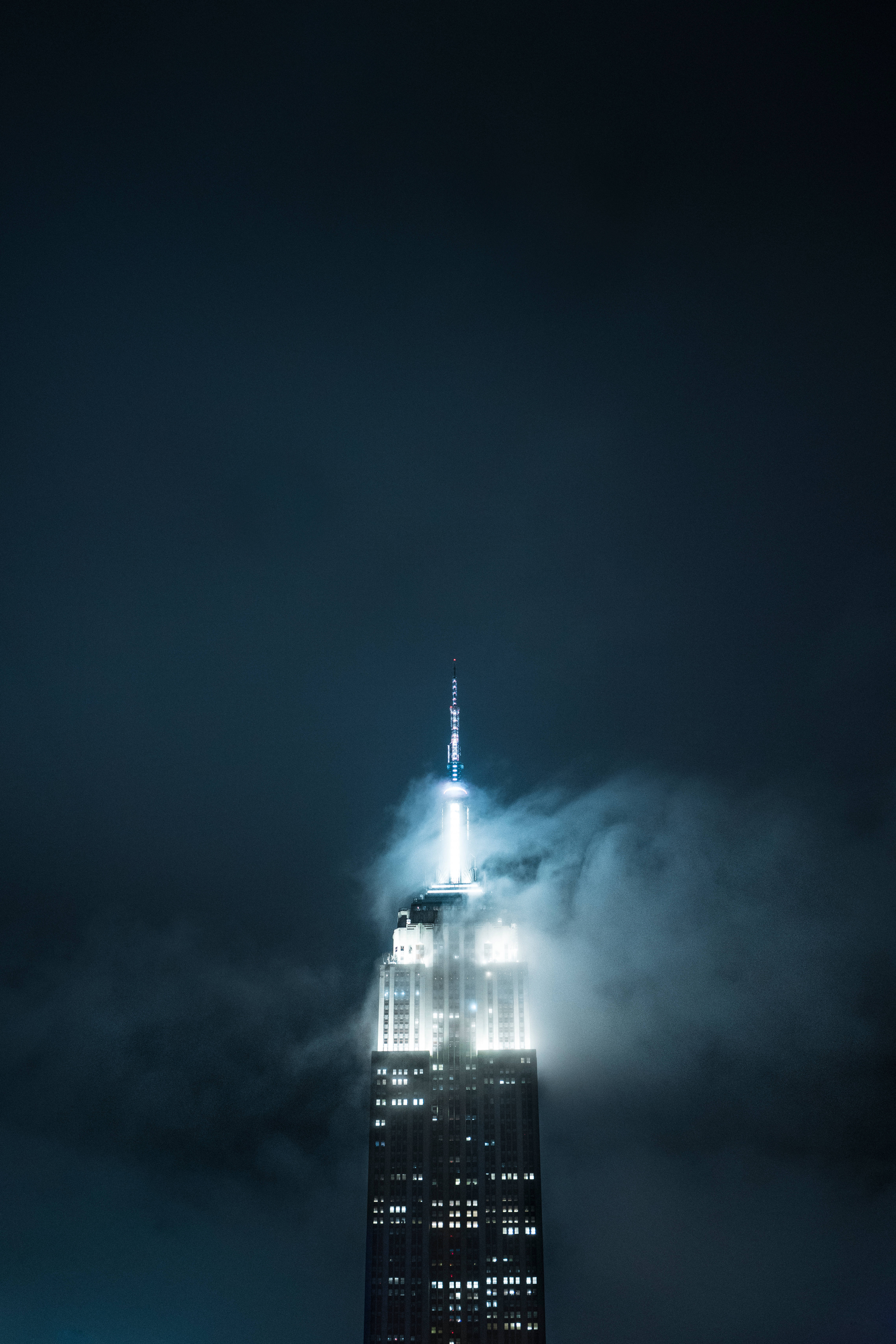 New 桌布 壁紙 — 帝國大廈刺穿黑暗多雲的夜空，其發光的尖頂在薄霧中閃耀。