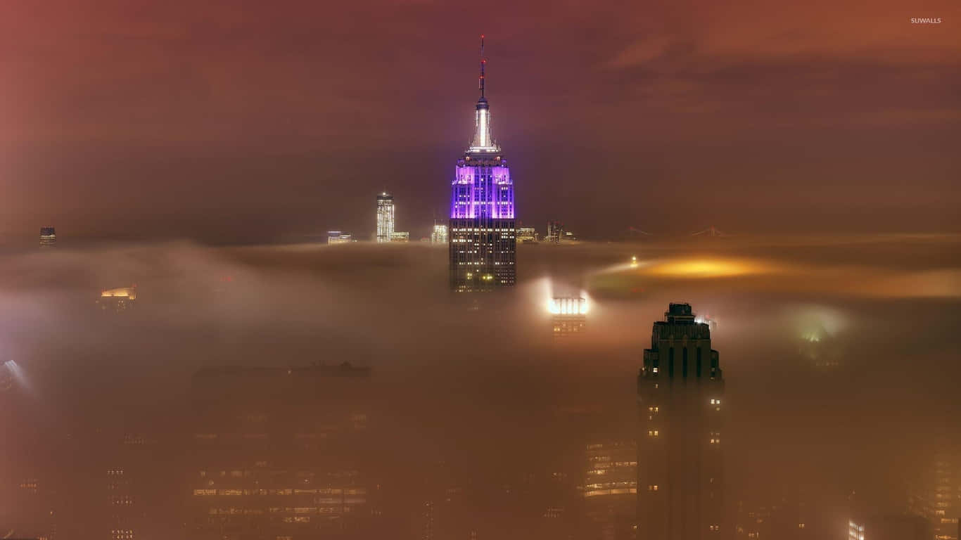 1366x768 Empire State Building 桌布 壁紙 — 帝國大廈在夜間穿透濃厚的橙色霧氣，其尖頂頂部發出紫色光芒。