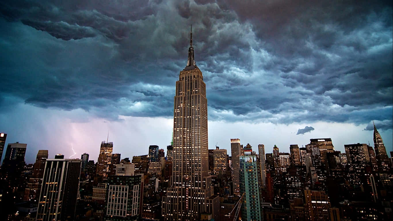 1366x768 Empire State Building 桌布 壁紙 — 帝國大廈在夜間紐約市天際線上閃電交加的戲劇性暴風雨天空下亮起。