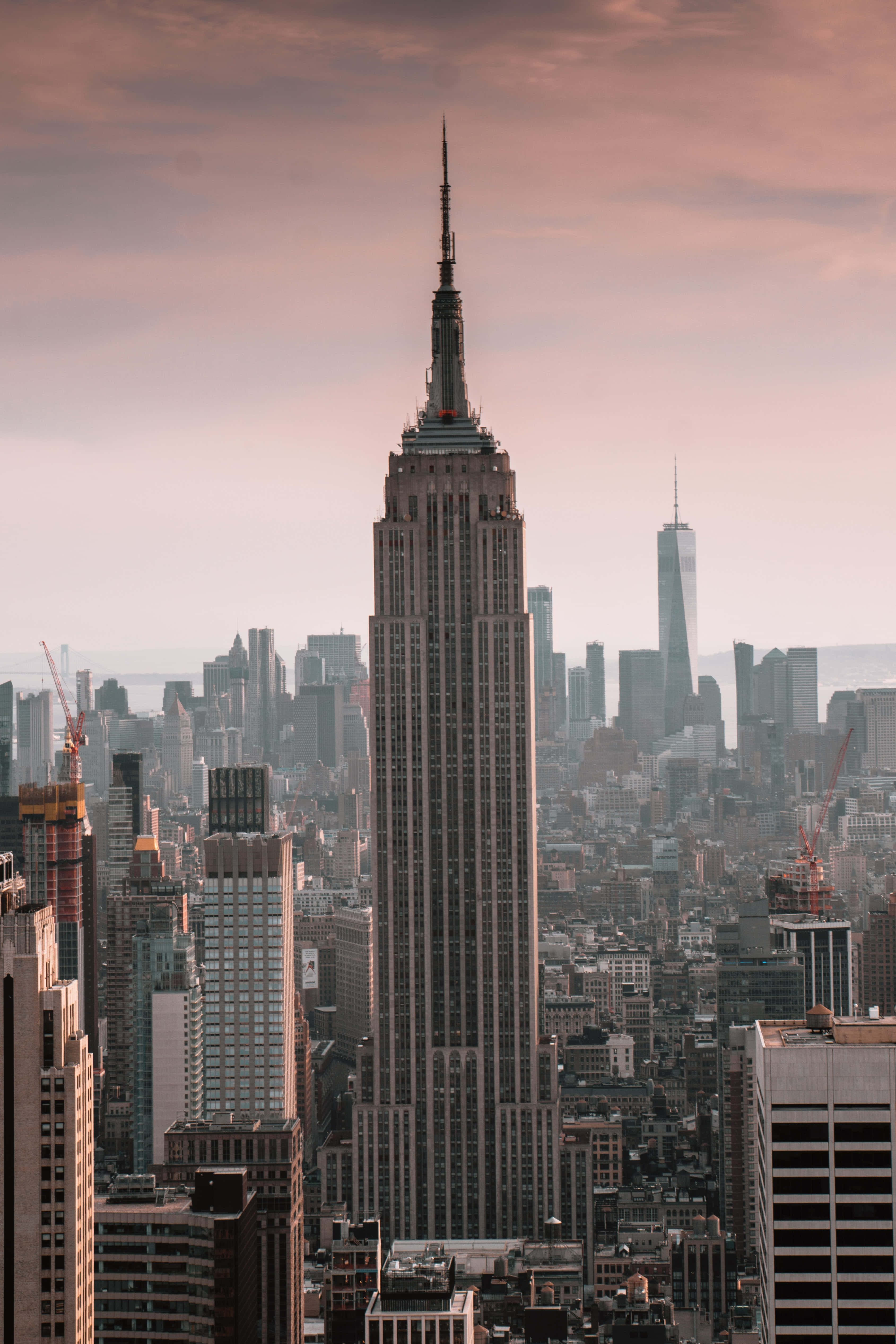 Empire State Building 桌布 壁紙 — 帝國大廈在日落時分以溫暖的粉紅色和橙色色調聳立在密集的紐約市天際線上。