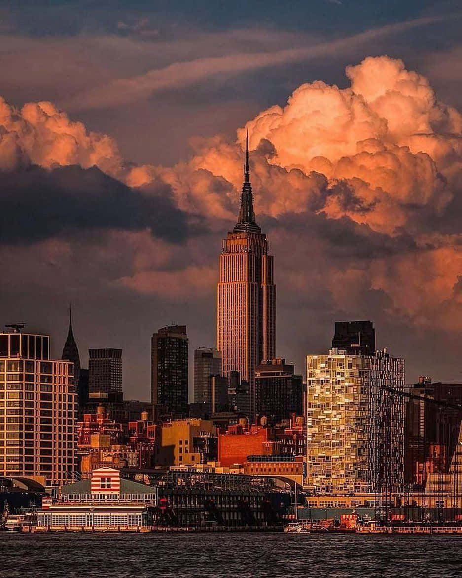 Nyc Aesthetic 桌布 壁紙 — 帝國大廈在日落時分聳立於紐約天際線之上，上方有火紅的橙色雲彩，下方有水。