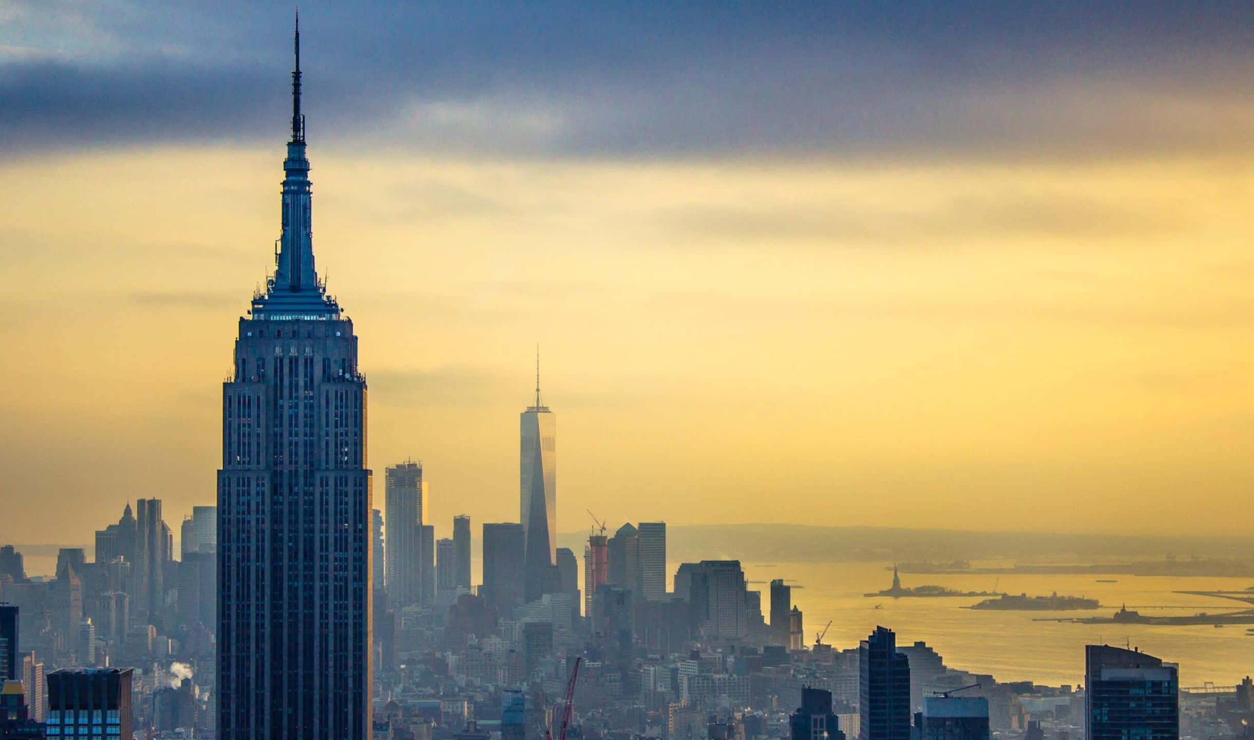 2440x1440 Empire State Building 桌布 壁紙 — 帝國大廈在日落時分聳立於紐約市上空，金色光芒沐浴著天際線和港口。