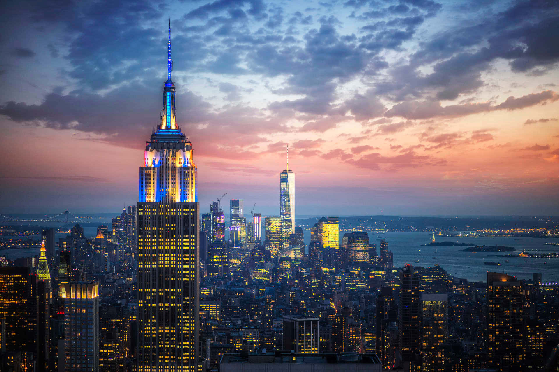 Nyc 桌布 壁紙 — 帝國大廈在暮色天空下亮起，粉橙色雲彩和下方閃爍的城市燈光。